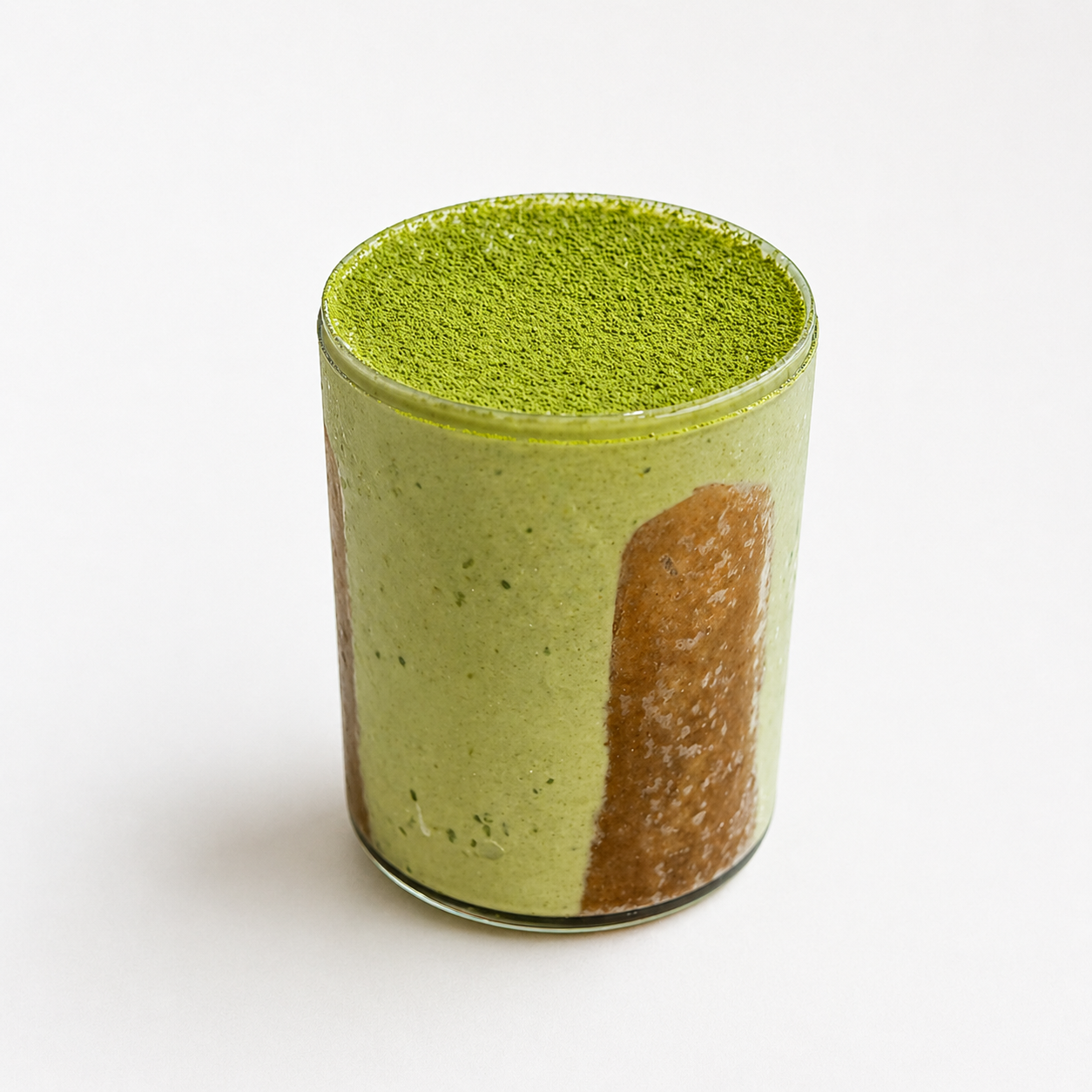 A glass of green matcha latte with a frothy top, sitting on a white surface.