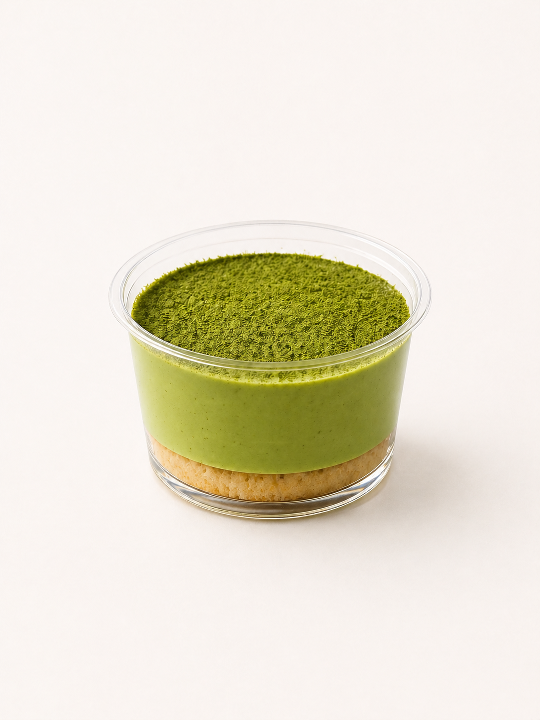 A layered dessert in a clear plastic cup with a crumbly base, a green mousse layer, and a textured green topping, possibly matcha.