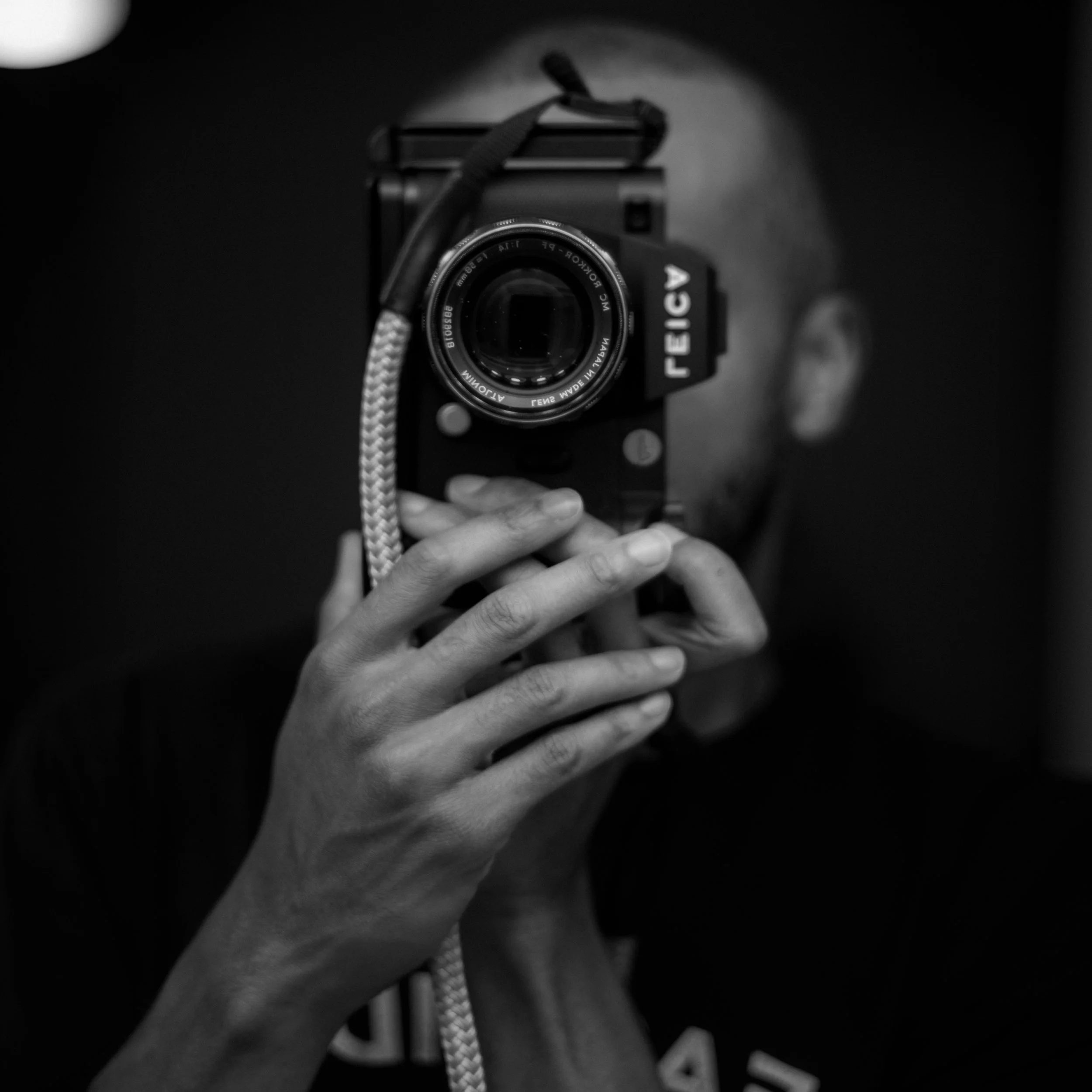 A person taking a black and white self-portrait using a camera reflected in a mirror, with their face partially obscured by the camera.