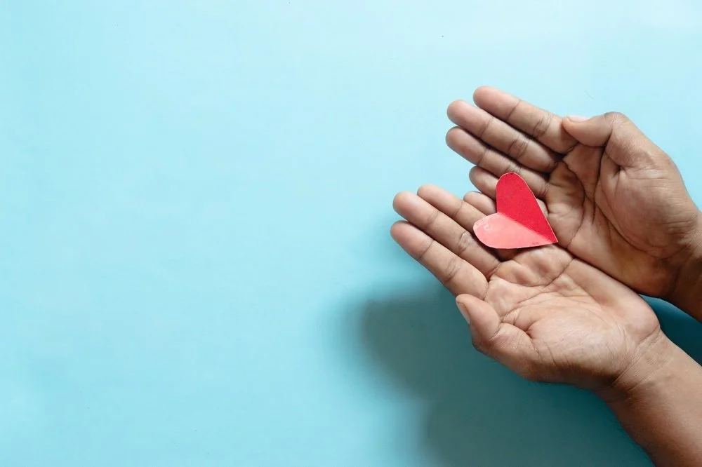 Open hands cradling a paper heart.