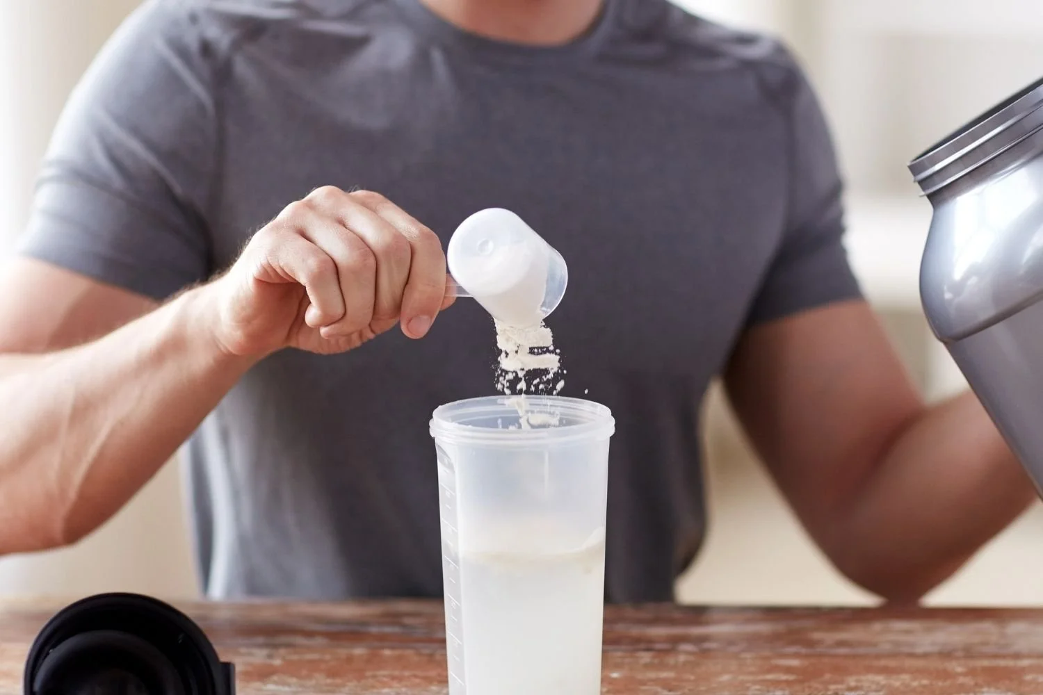 Person adding creatine powder to a shaker bottle for performance and recovery