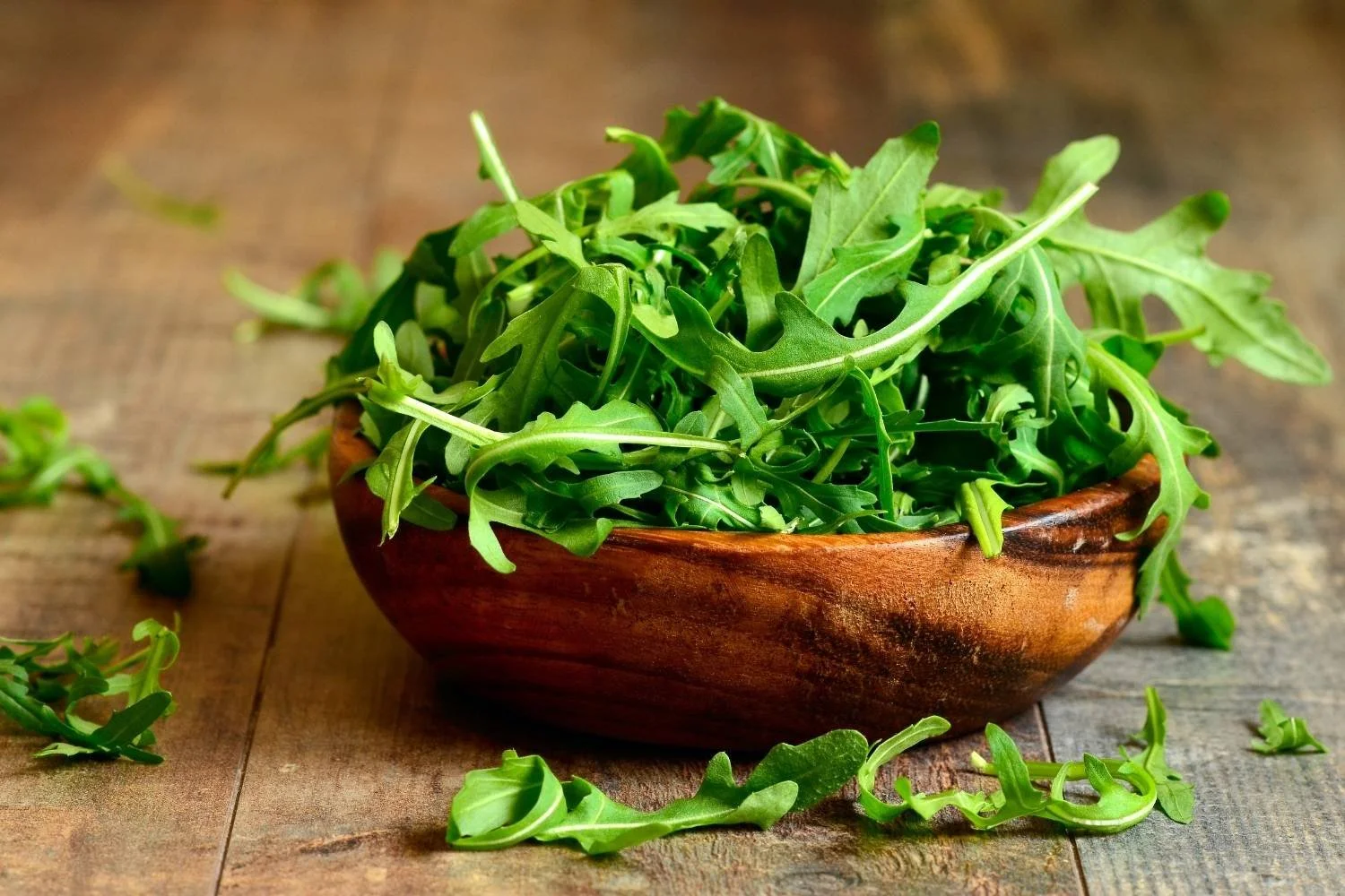 A wooden salad bowl filled with fresh, green arugula leaves.