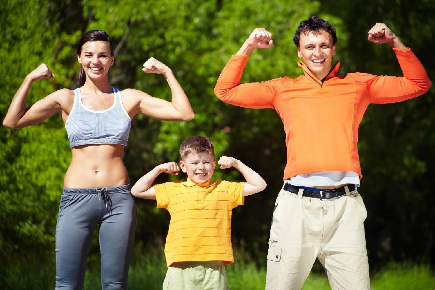 Smiling mother, father, and young son flexing their arms together outdoors in the sunshine.