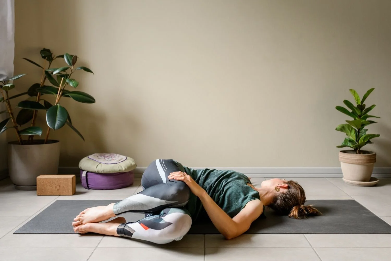 Woman lying on her back on the floor with bent knees lowered to one side in a supine twist.