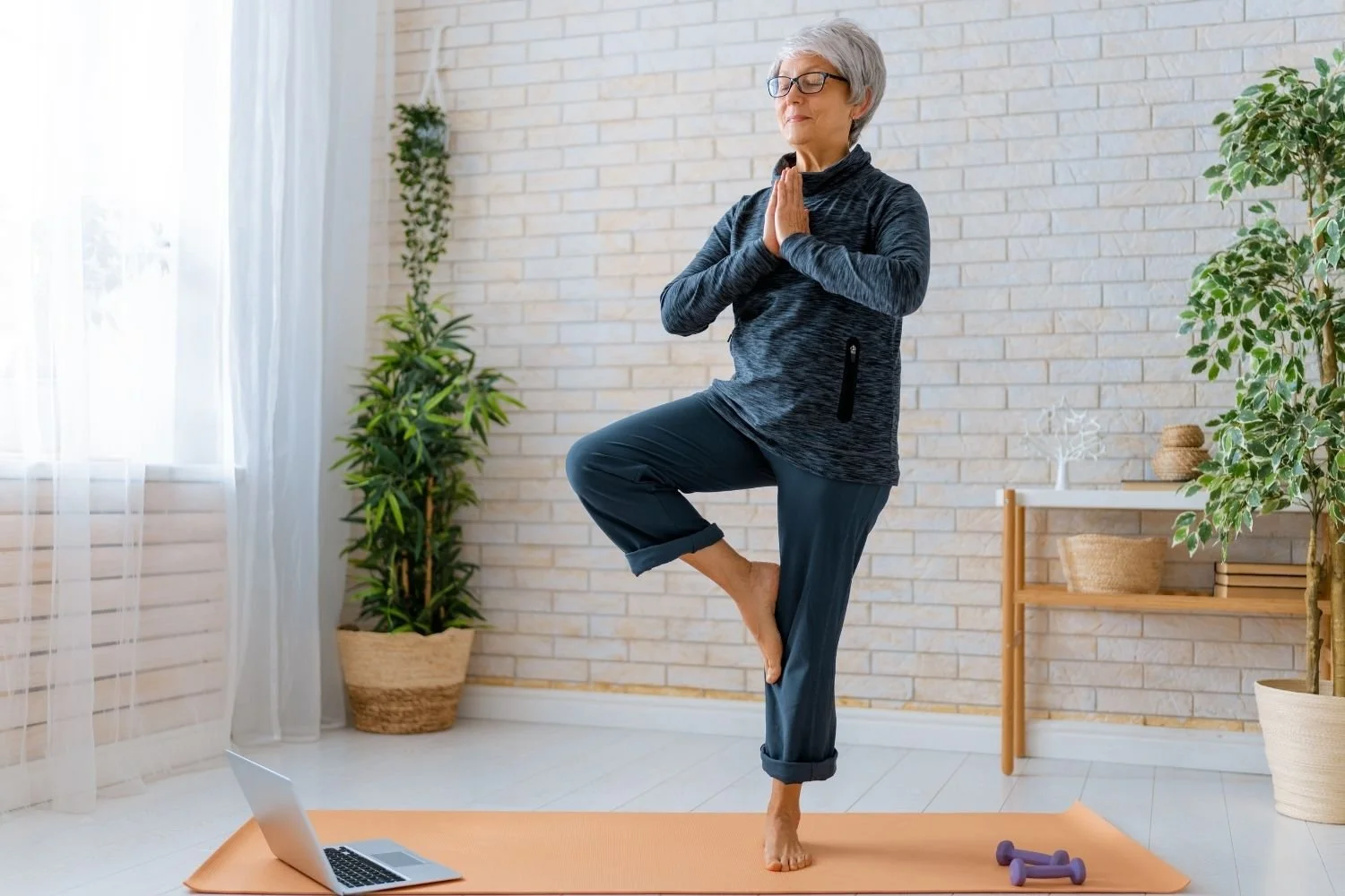 Older woman practicing a balance yoga pose at home, demonstrating balance and mobility training for healthy aging