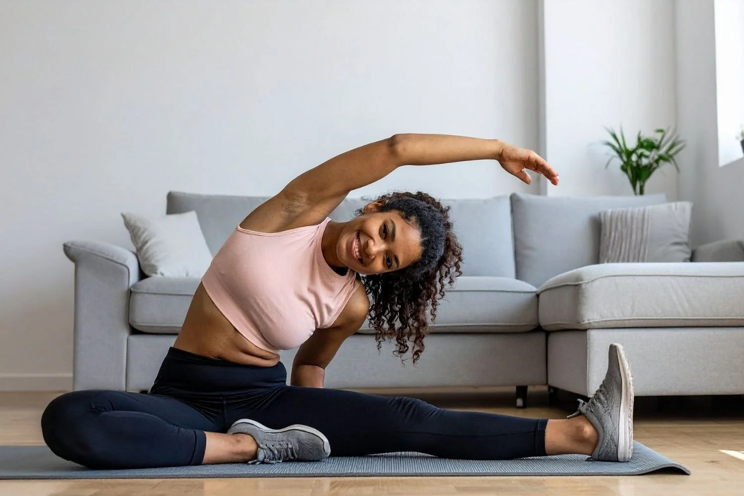 Woman performing a seated stretch on a yoga mat at home, representing recovery and lifestyle practices for long-term fitness