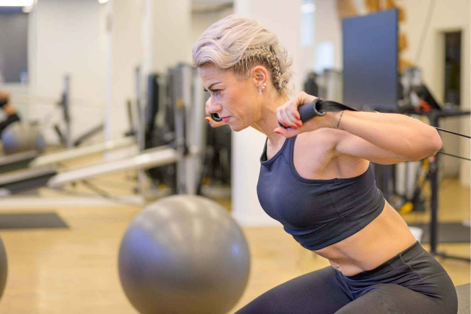 Fit middle-aged woman performing a cable resistance exercise in a gym, demonstrating strength training for lifelong fitness