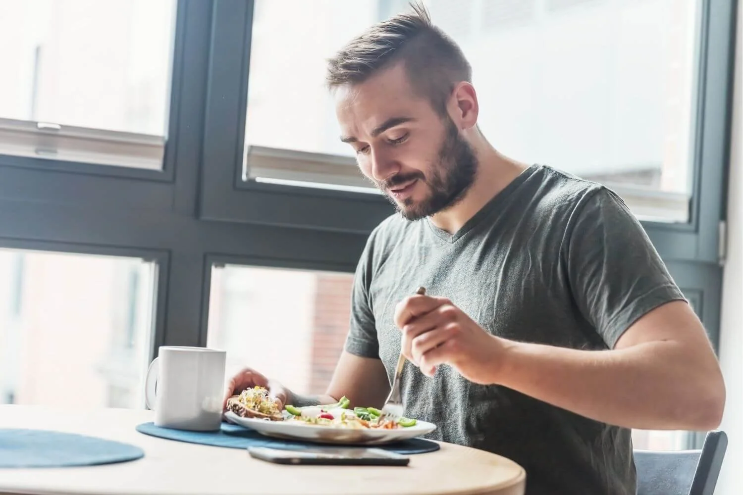Man eating a balanced plate of eggs, toast, and vegetables at a kitchen table, illustrating a protein-rich meal as part of a daily diet