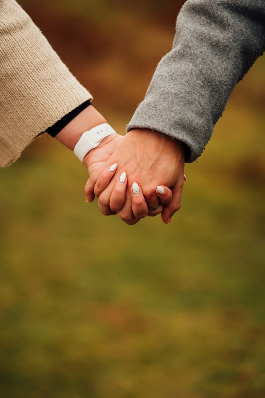 Two people holding hands outdoors, wearing long sleeves and the person on the left has a white wristwatch.