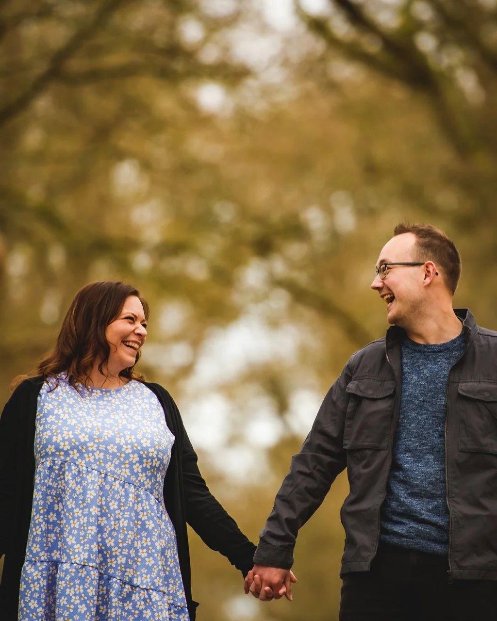 A couple holding hands and laughing outdoors in a park during autumn.