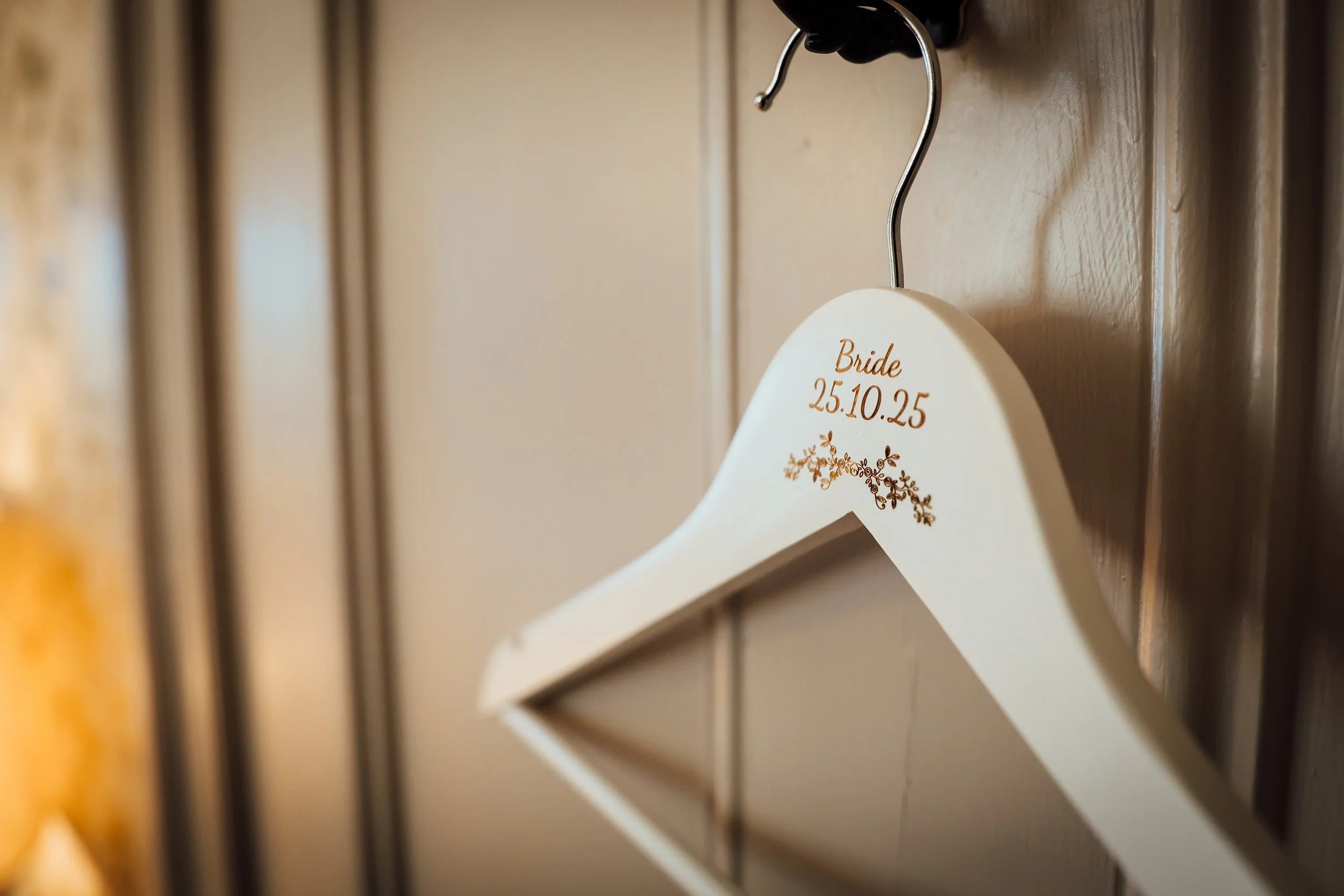Wedding hanger with the date 25.10.25 and the word Bride, hanging on a hook on a wooden wall.