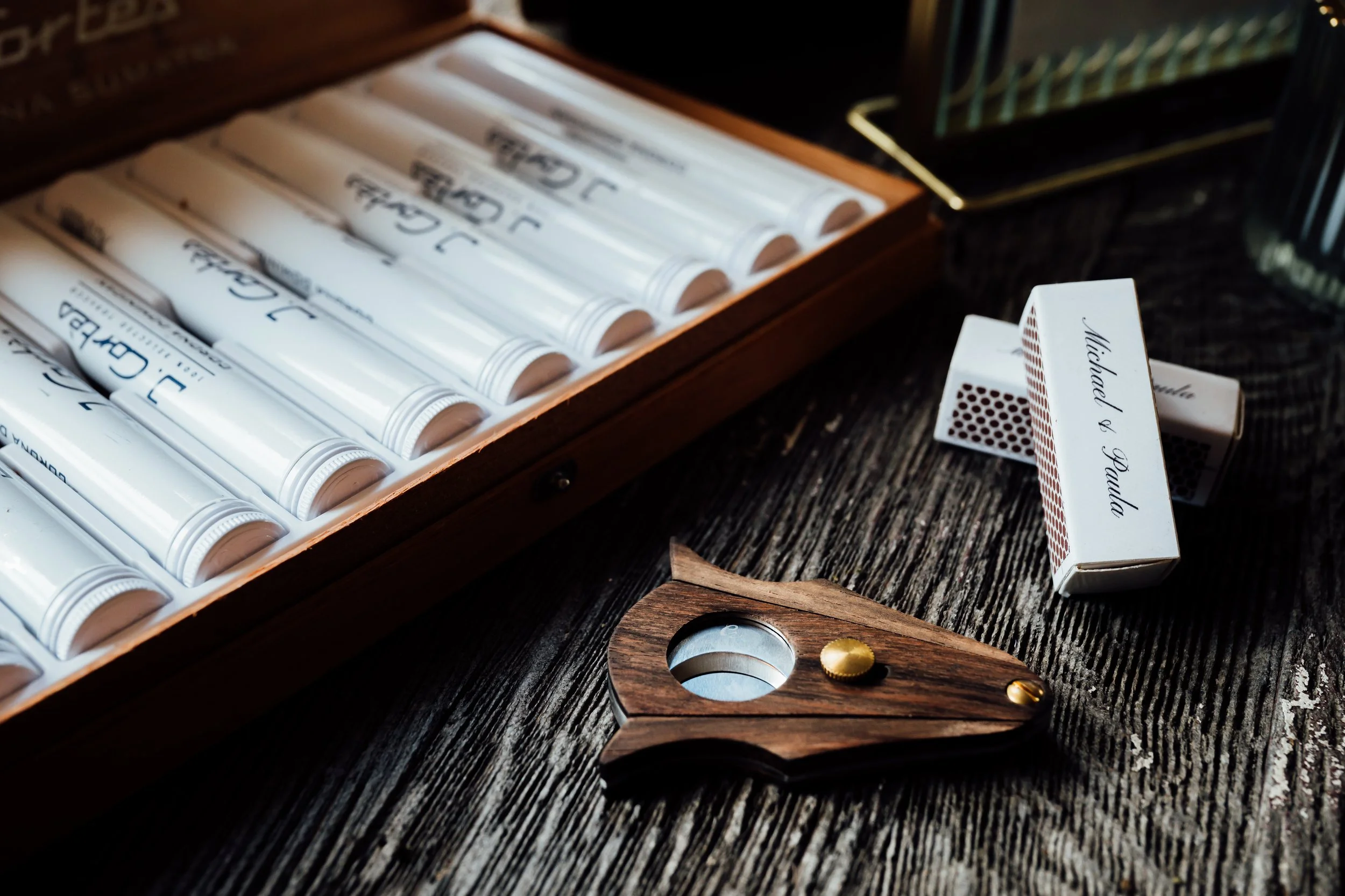 A wooden table with a box of white tubes of paint, a wooden magnifying glass with a brass screw, and two boxes of playing cards labeled 'Michaela & Paul'.