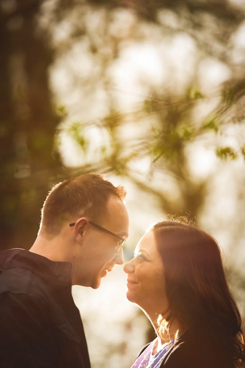 A man and woman face each other closely outdoors at sunset, smiling.