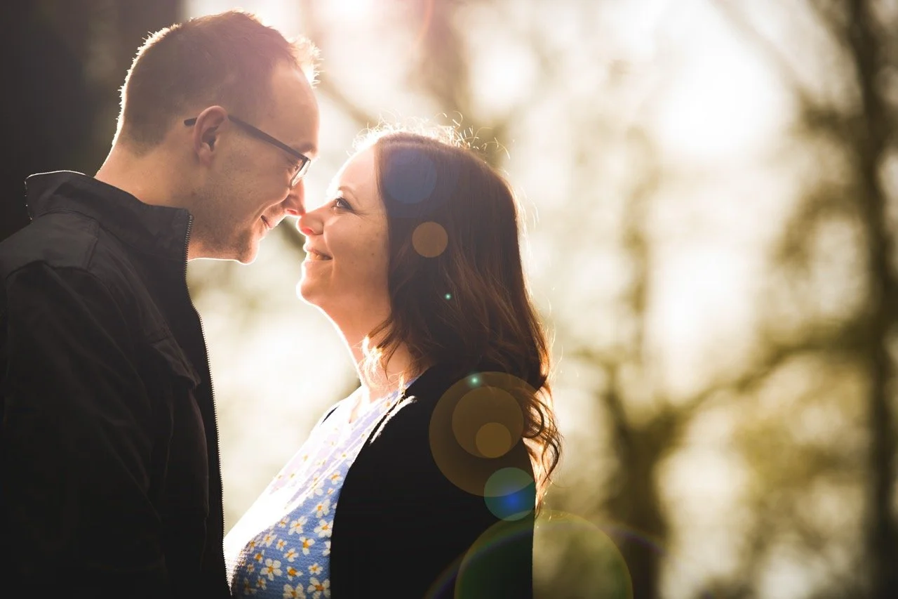 A man and woman face each other smiling outdoors with sunlight behind them, creating a warm glow.