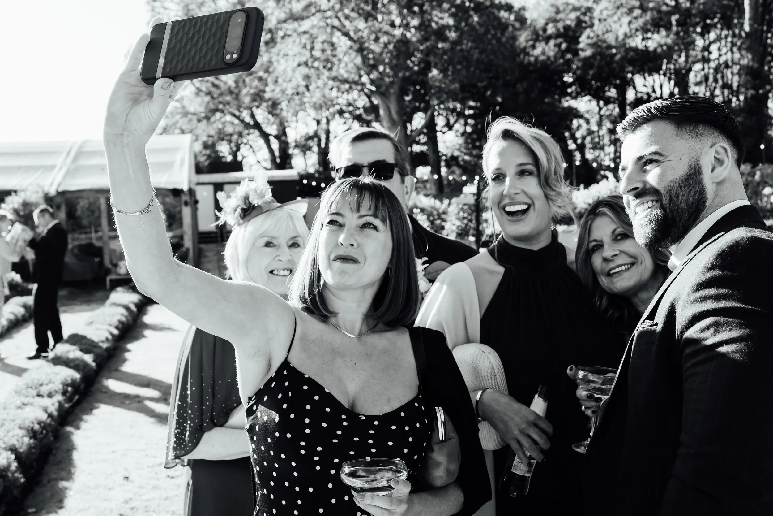 Group of friends taking a selfie together at an outdoor celebration, holding drinks and smiling.