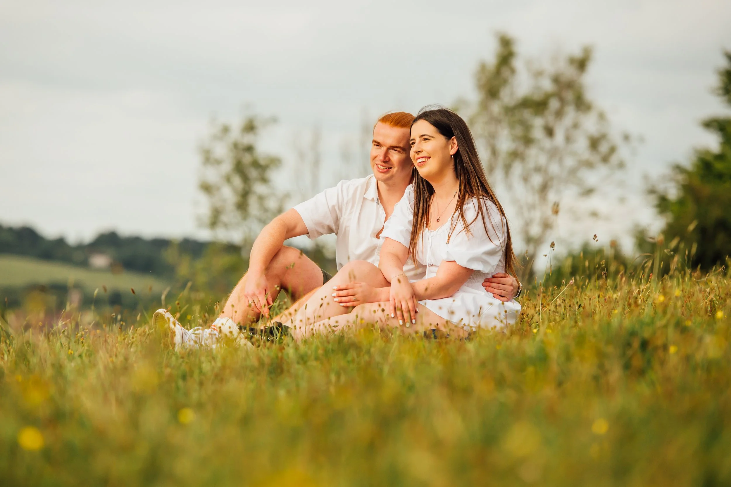 A young couple sitting on a grassy field, smiling and enjoying a moment together outdoors.
