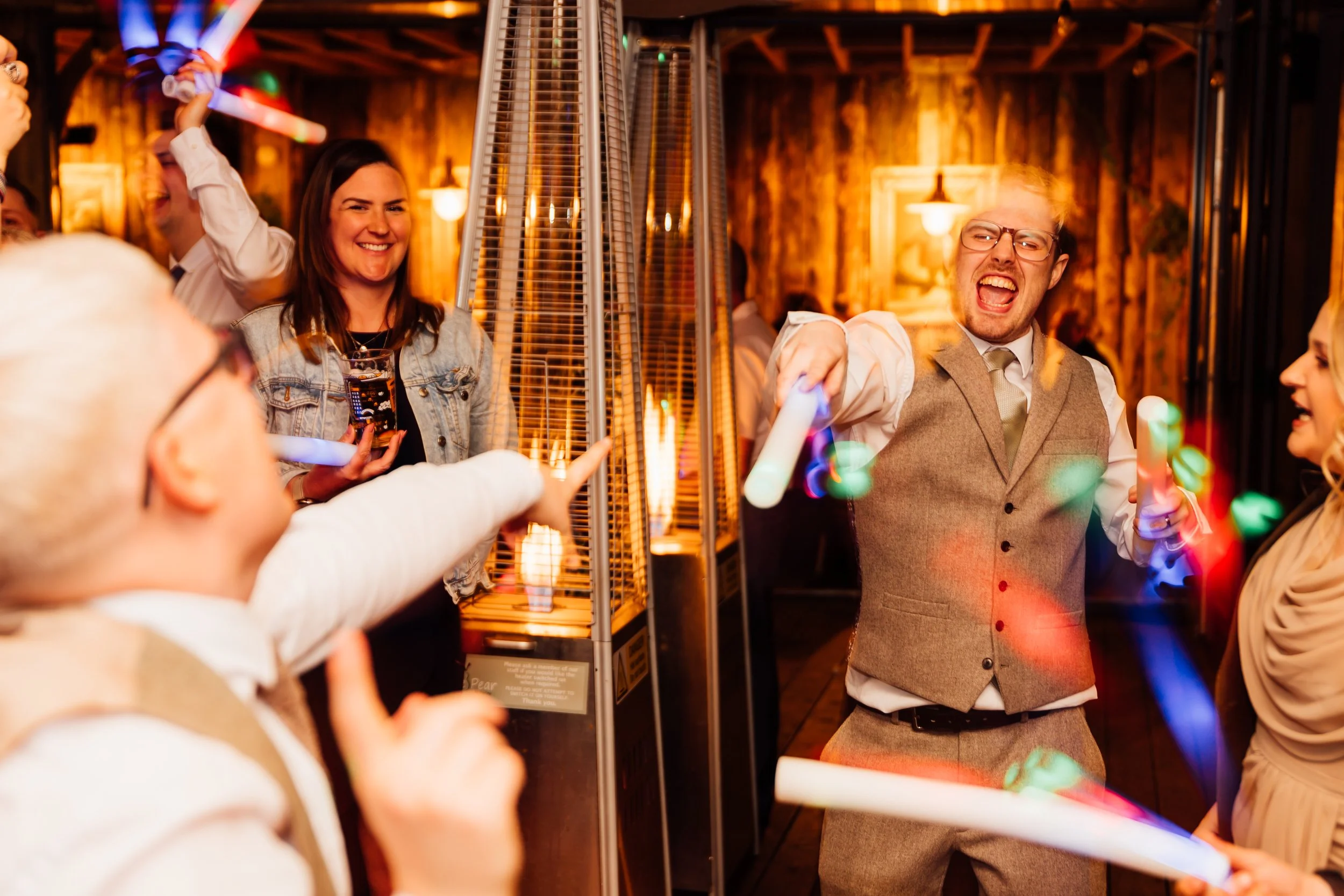 Group of people celebrating indoors with glow sticks and drinks, smiling and dancing