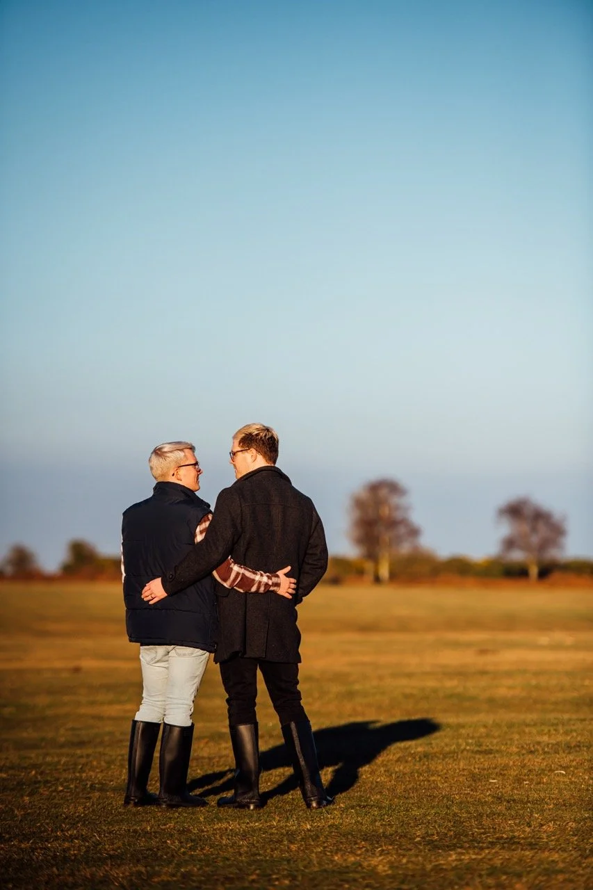 Two men standing close together on a grassy field, having a conversation at sunset, with few trees in the background.