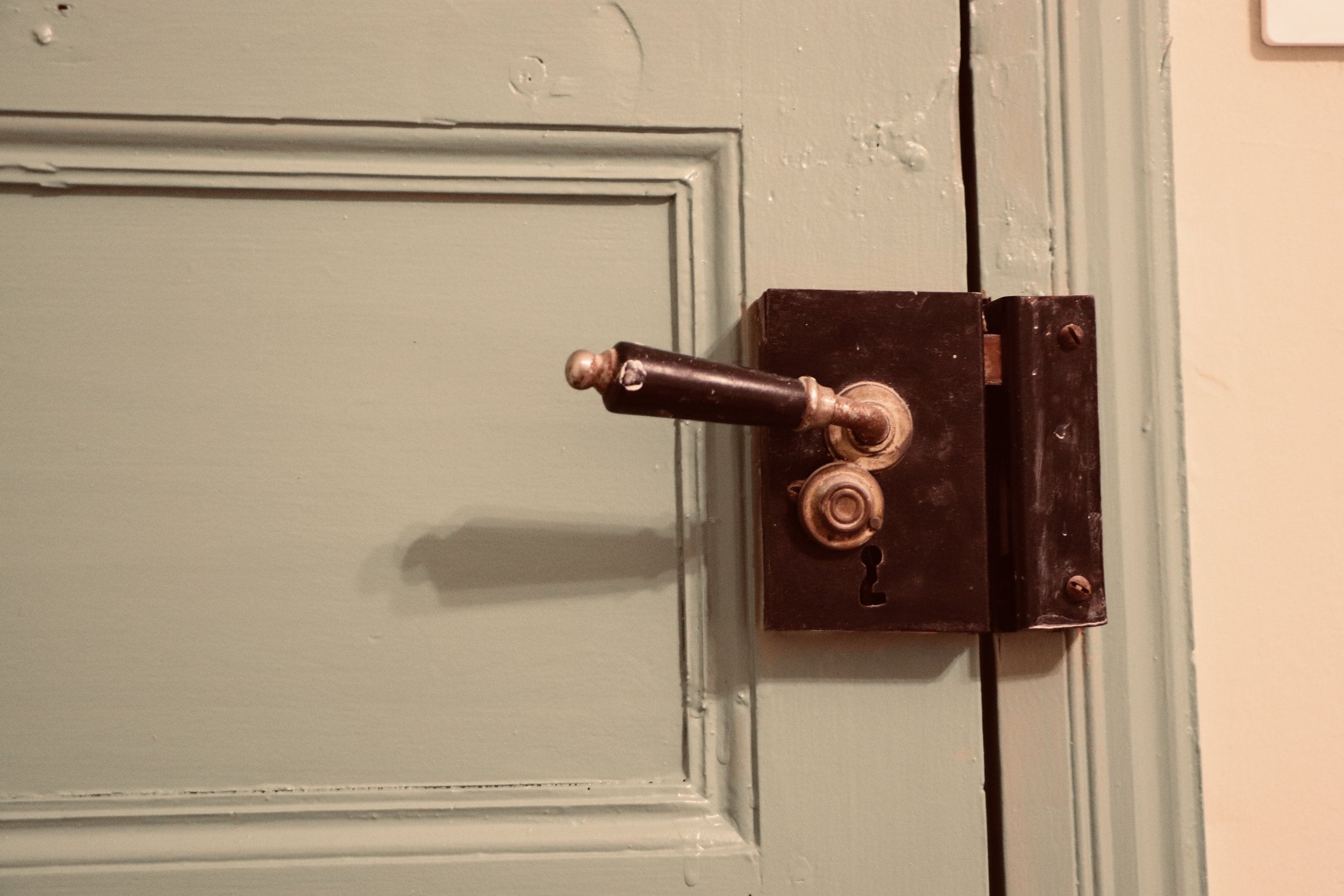 Poignée de porte ancienne en cuivre sur une porte en bois peint en vert clair.