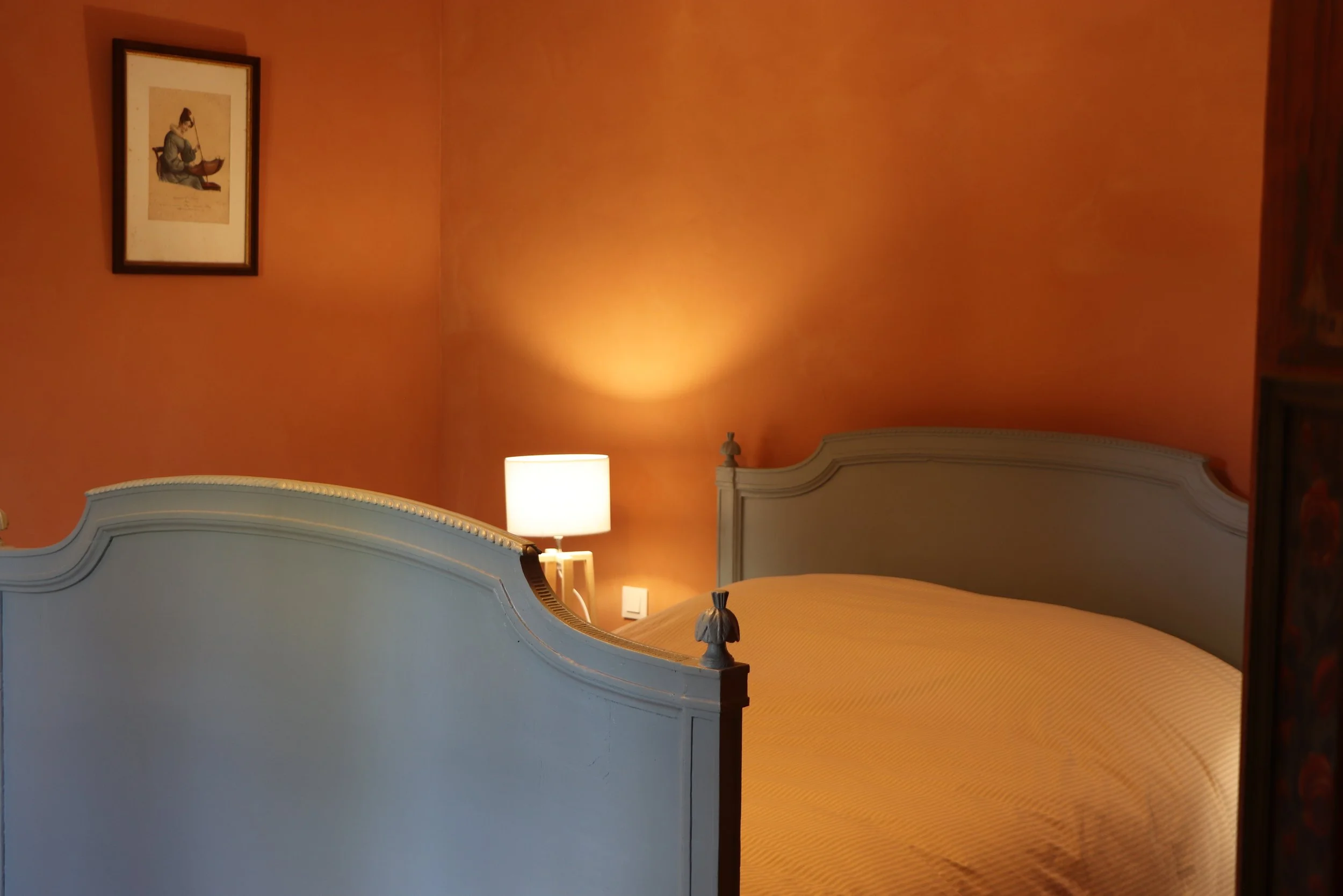 Chambre avec lit double, lampadaire allumé, murs orange, tableau encadré au mur.