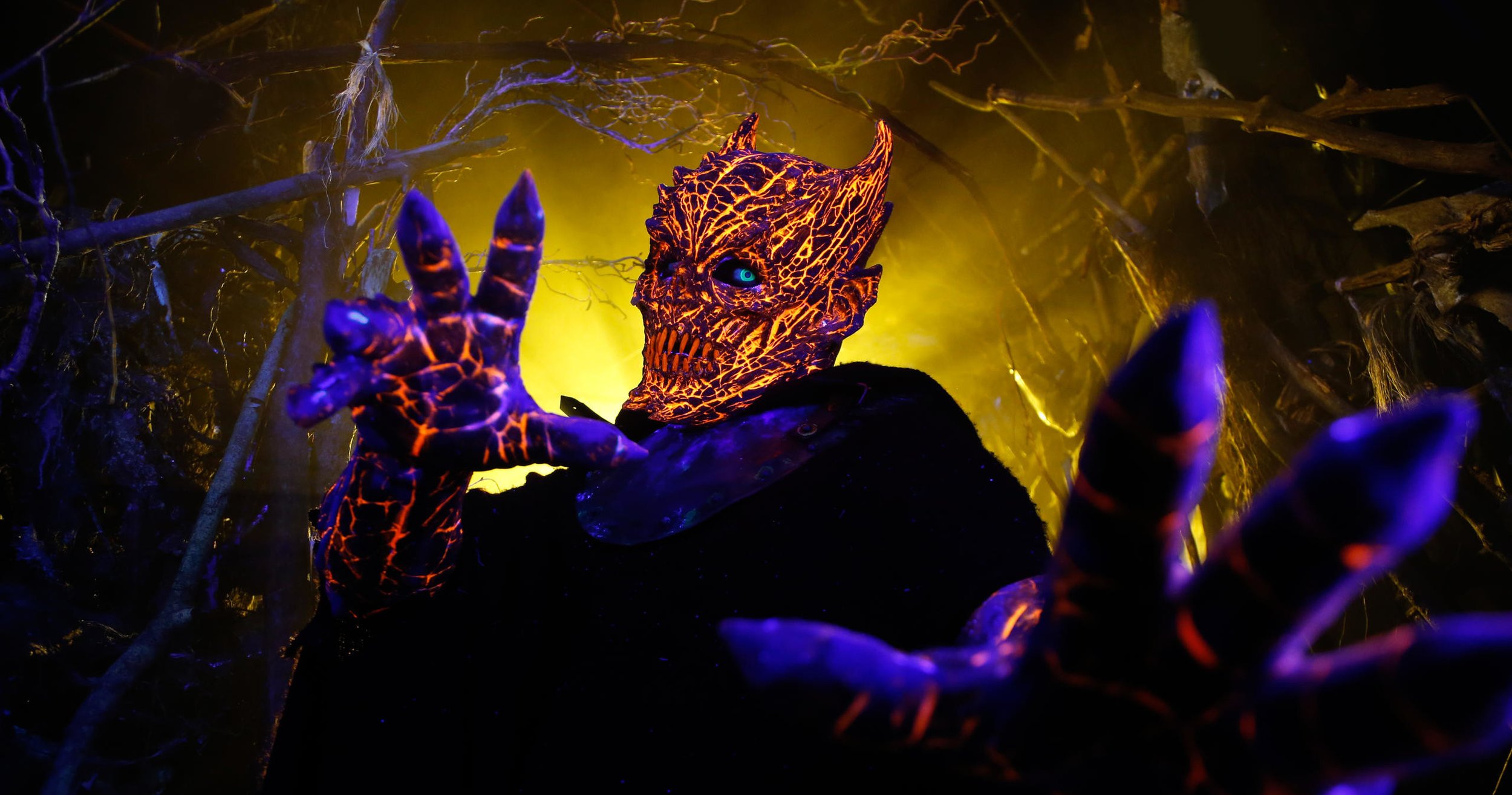 Creature with glowing orange and purple cracked skin and horns, set against a dark forest background with yellow lighting.