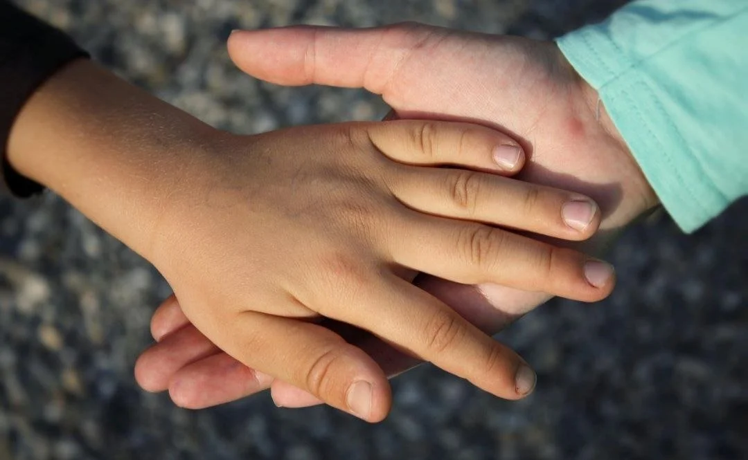 Zwei Kinderhände, eine helle und eine dunkle, berühren sich an den Fingern im Außenbereich.