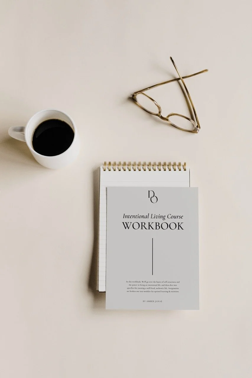 Top view of a coffee cup, eyeglasses, and an "Intentional Living Course Workbook" on a spiral notebook on a light surface.