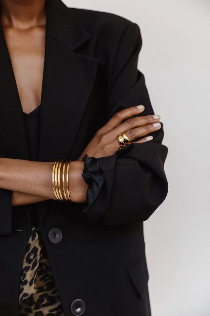 Woman in black blazer with gold bracelets and rings
