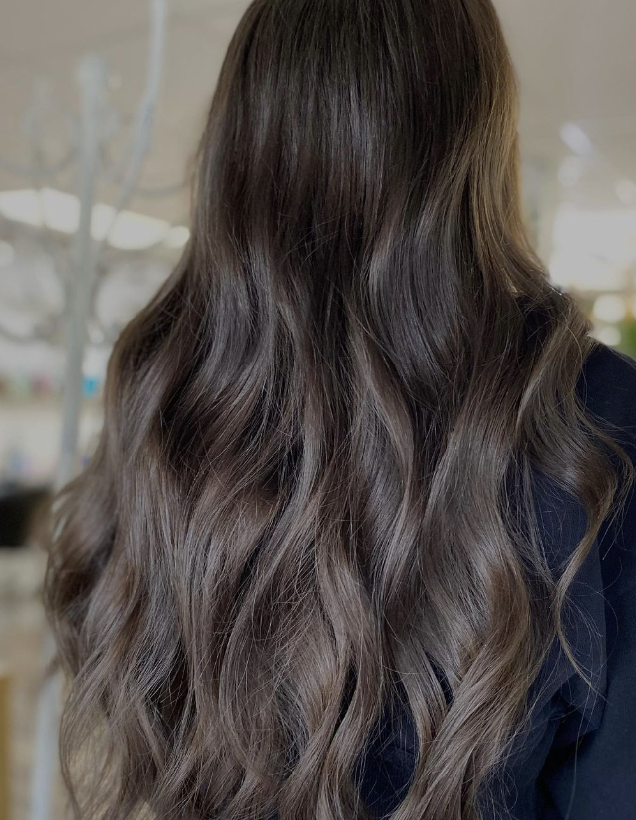 Woman with long wavy hair featuring a gradient from dark brown to ash blonde, styled in loose waves.