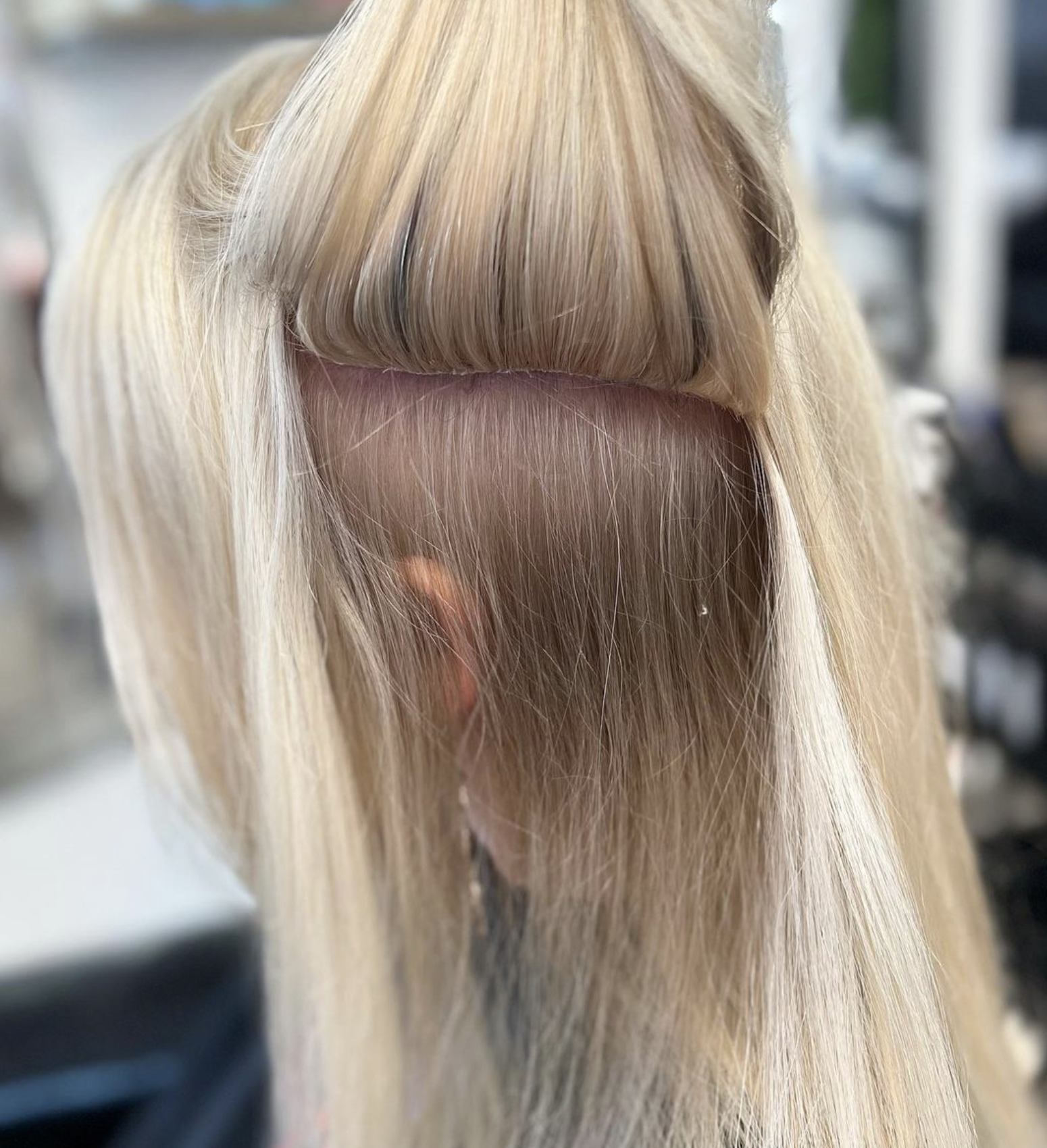 Close-up of a person's head with blonde hair and bangs, showing a section of the scalp and hair roots.