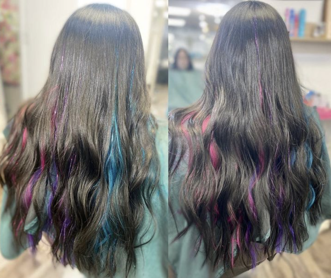 Back view of a woman with long, wavy brown hair featuring streaks of pink, purple, blue, and teal highlights.
