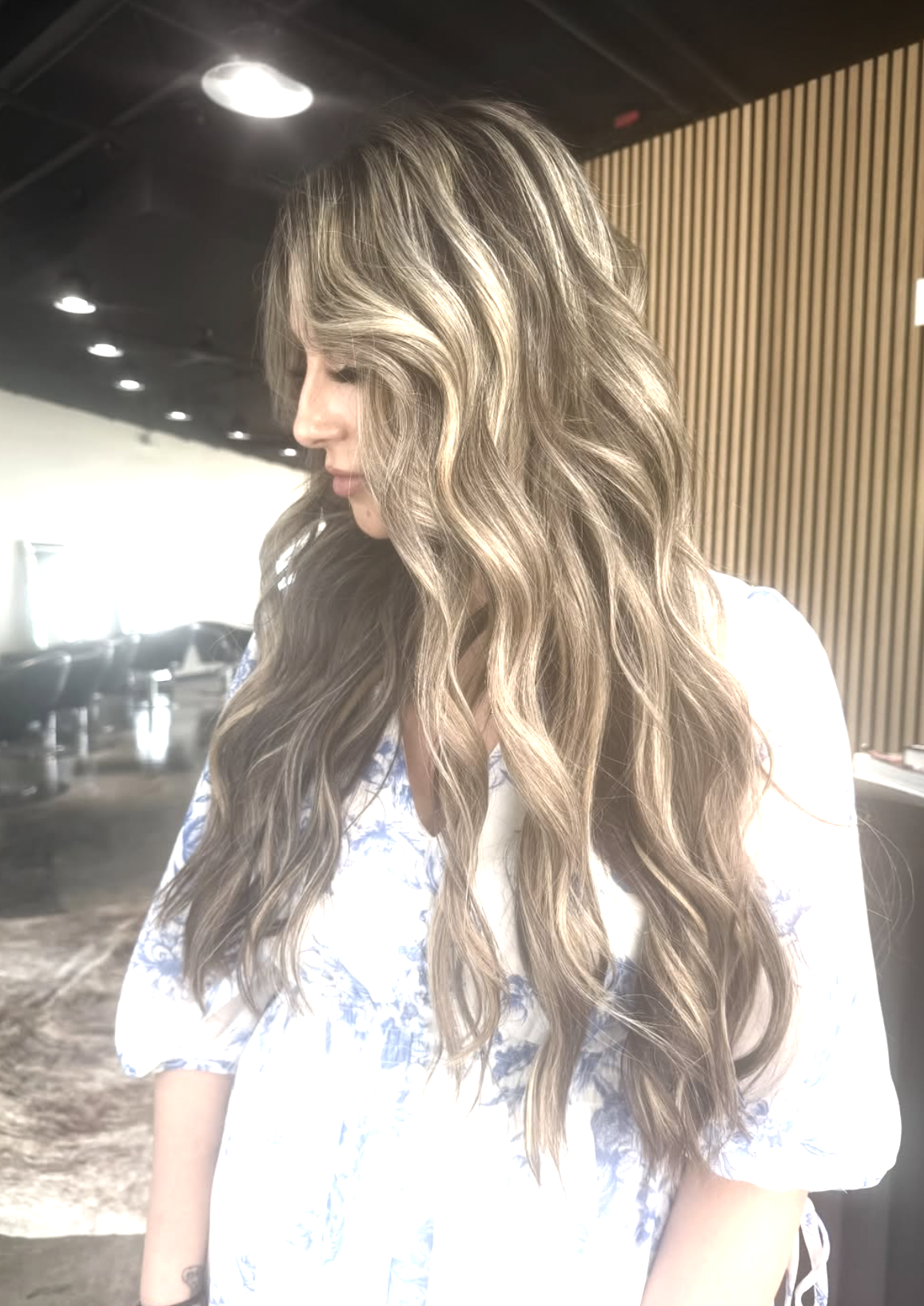 Woman with long, wavy, blonde hair in a modern interior setting.