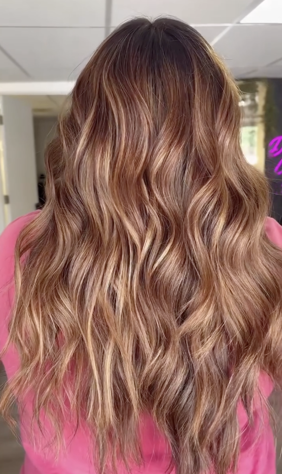 Back view of a woman's wavy, long hair with caramel highlights.