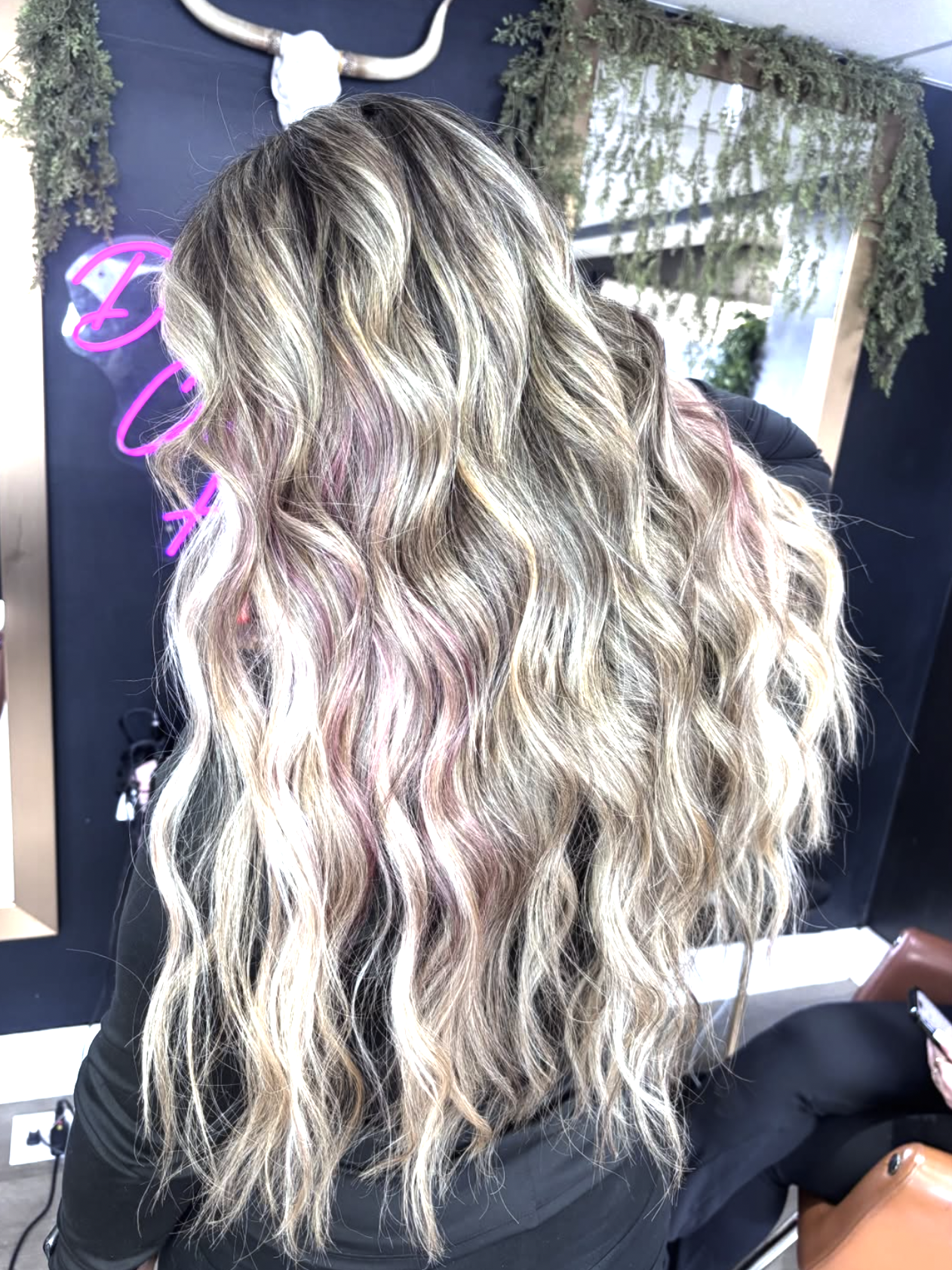 Long wavy hair with blonde, pink, and darker highlights in a salon setting.