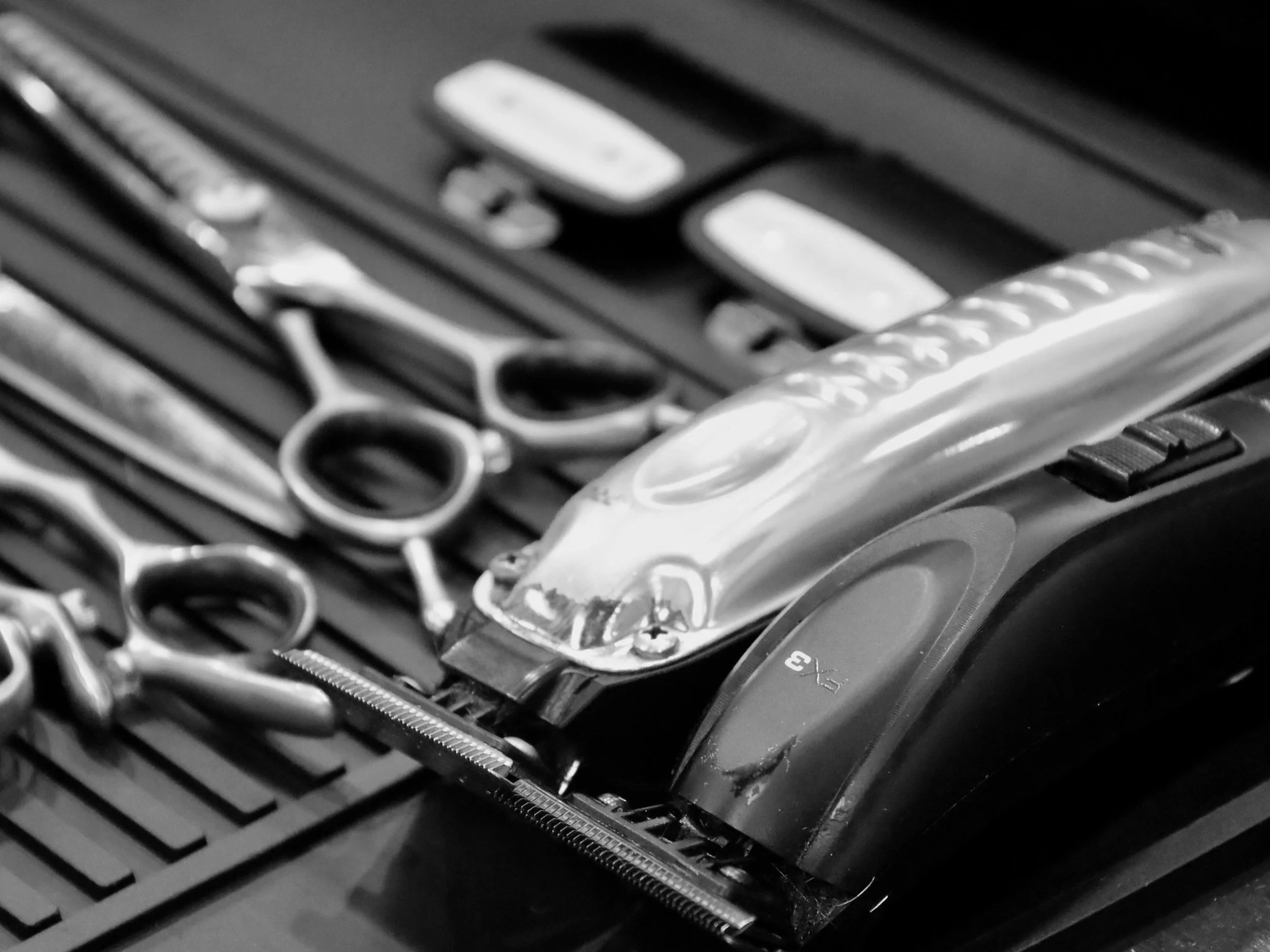 A collection of barber or hairstyling tools including scissors and hair clippers on a textured surface.