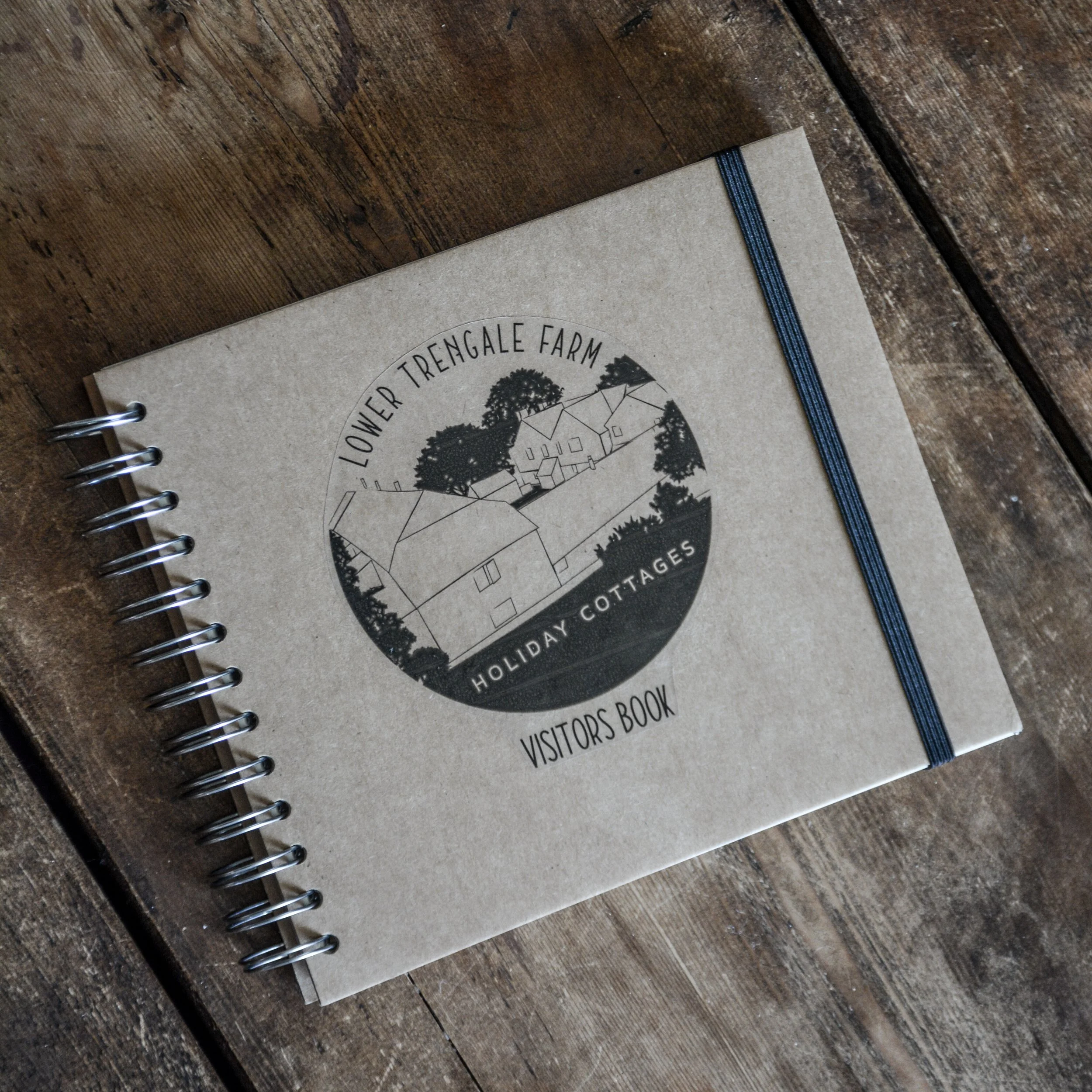 A spiral-bound visitors book titled 'Lower Trengale Farm Holiday Cottages' placed on a wooden surface.