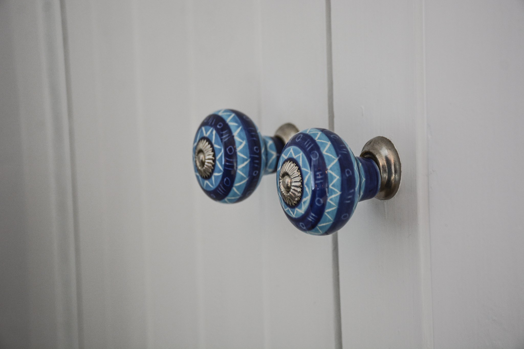 Close-up of two decorative blue door knobs on a white door.
