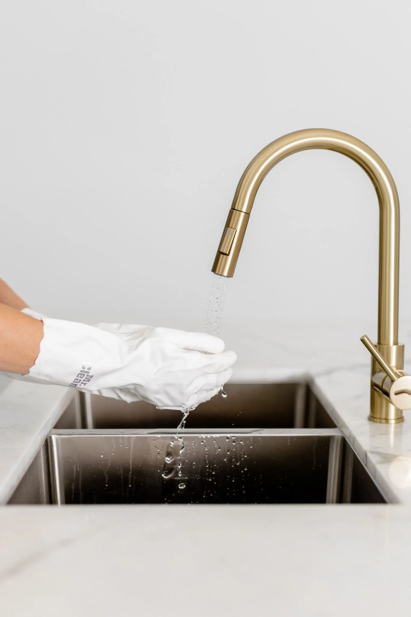 Person wearing white gloves washing hands under a gold kitchen faucet.