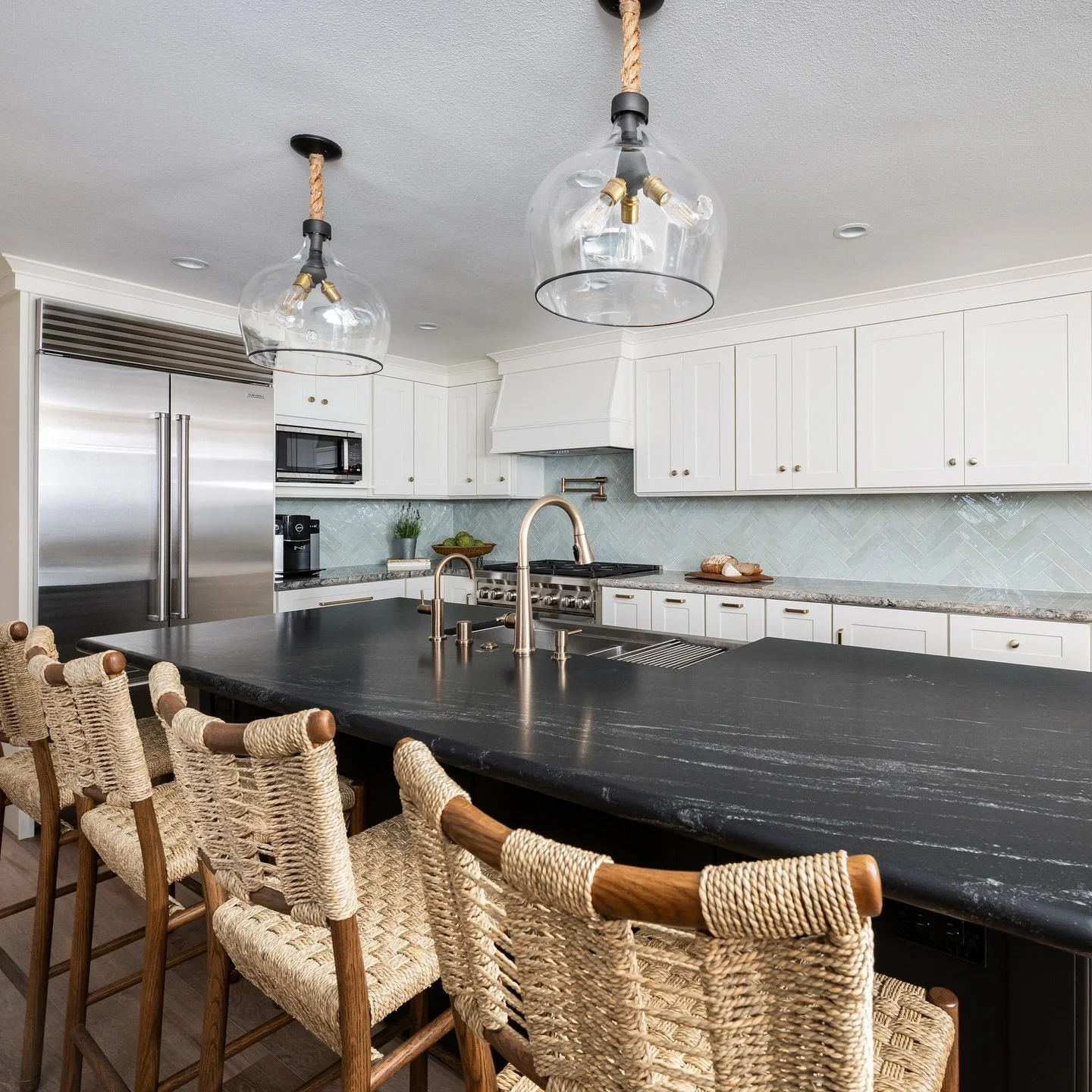 Old love, new flame. We kept our client&rsquo;s beloved granite countertops on the perimeter (because some classics never go out of style) and paired them with a complimentary bold black island topped in a sleek new surface. Add the seaglass tile bac