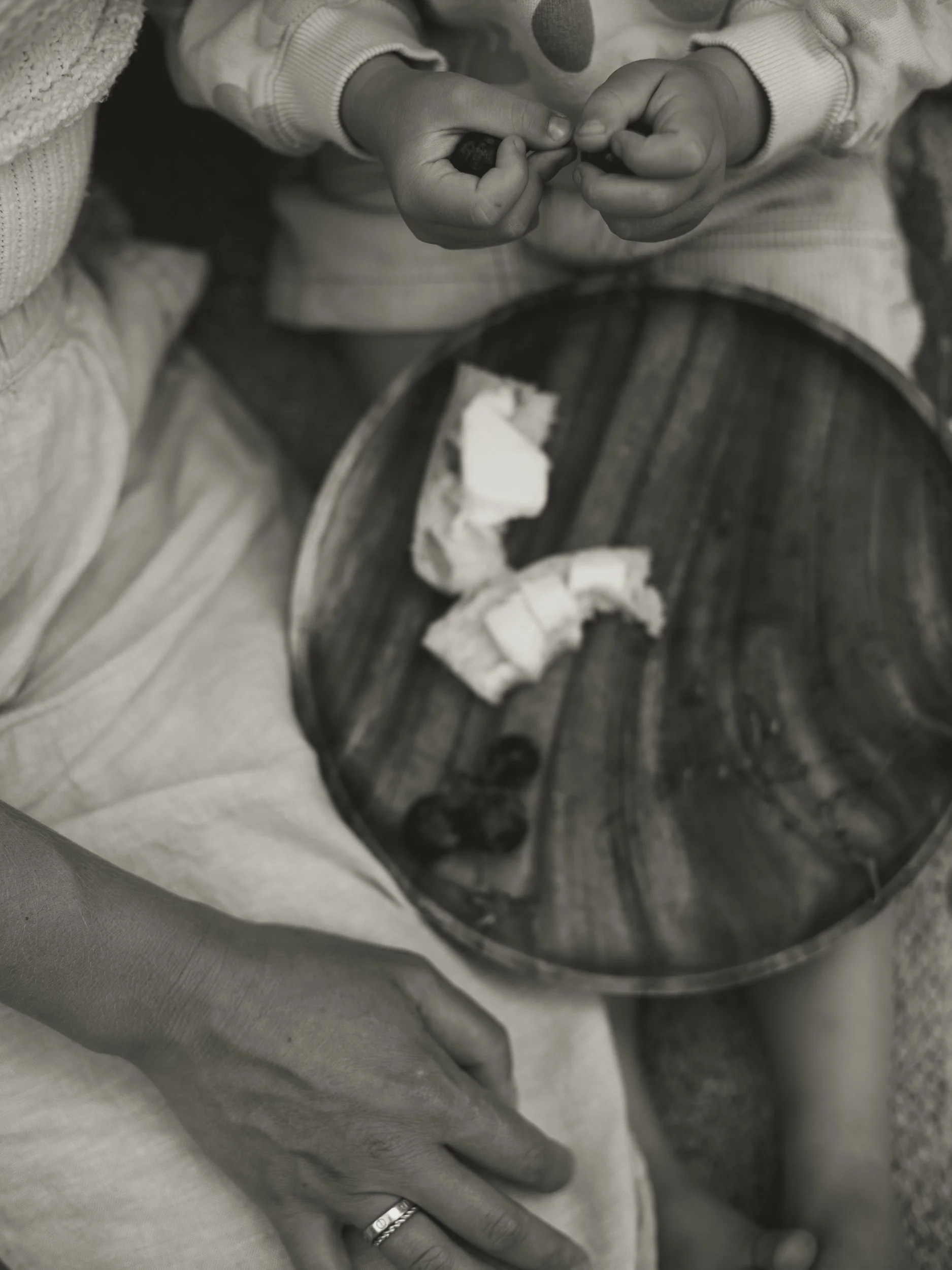 A person is holding hands with a child. There is a bowl with some bread crumbs and blueberries on the person's lap.