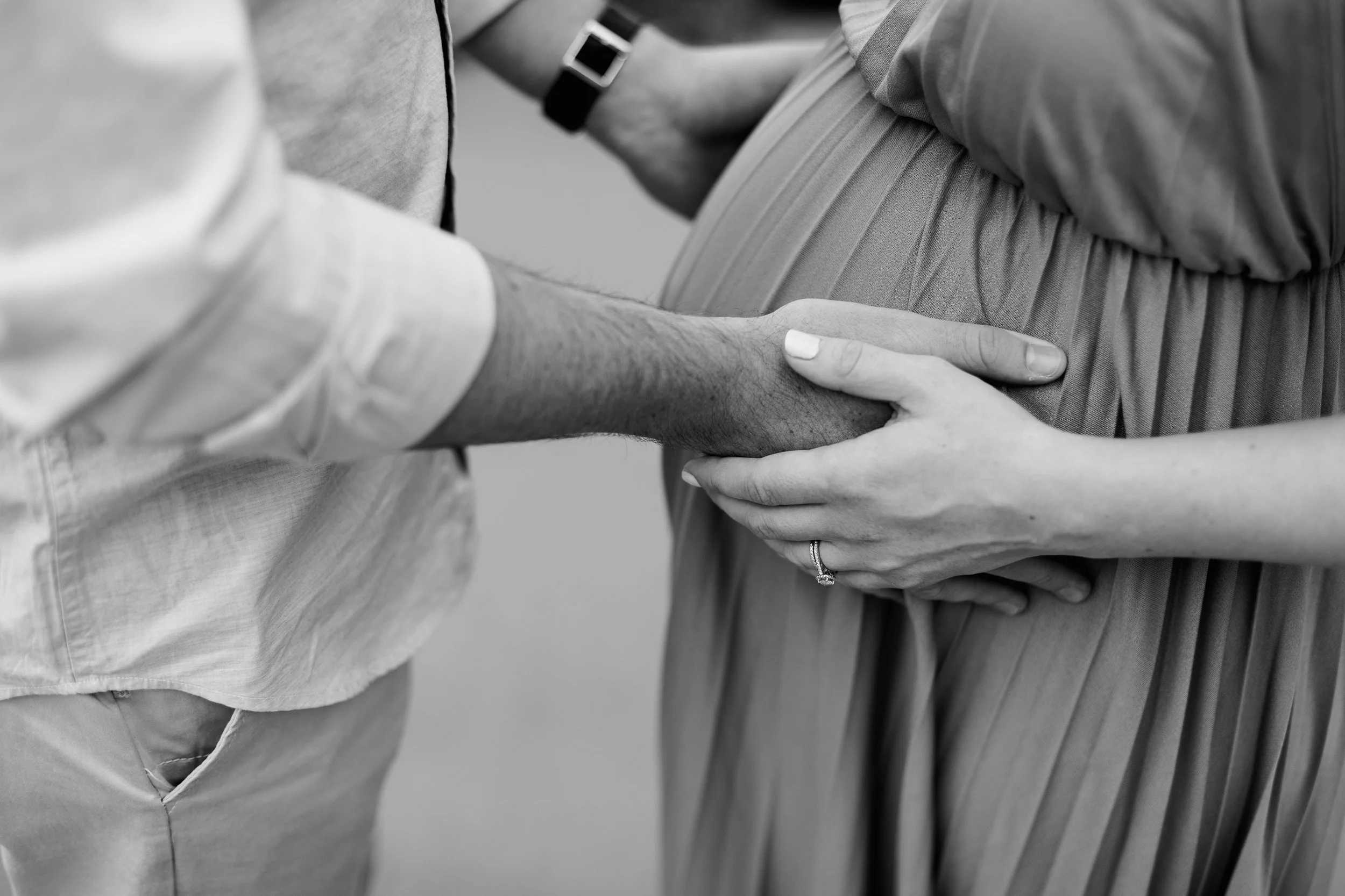 A man and woman, with the woman pregnant, holding hands in a close-up black and white photograph.