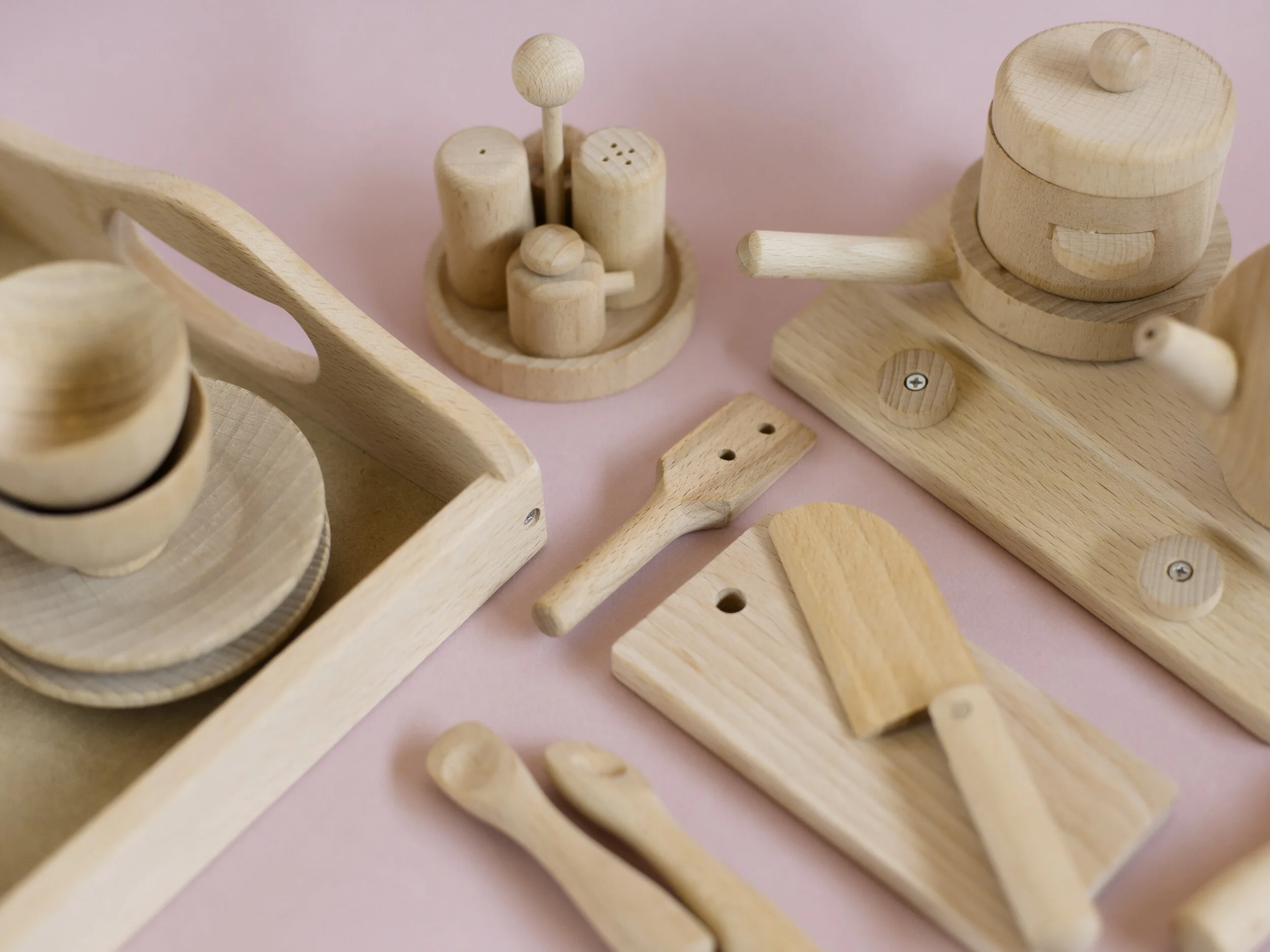 Wooden toy tools including a hammer, screwdriver, saw, and various small blocks and pieces, arranged on a pink surface.