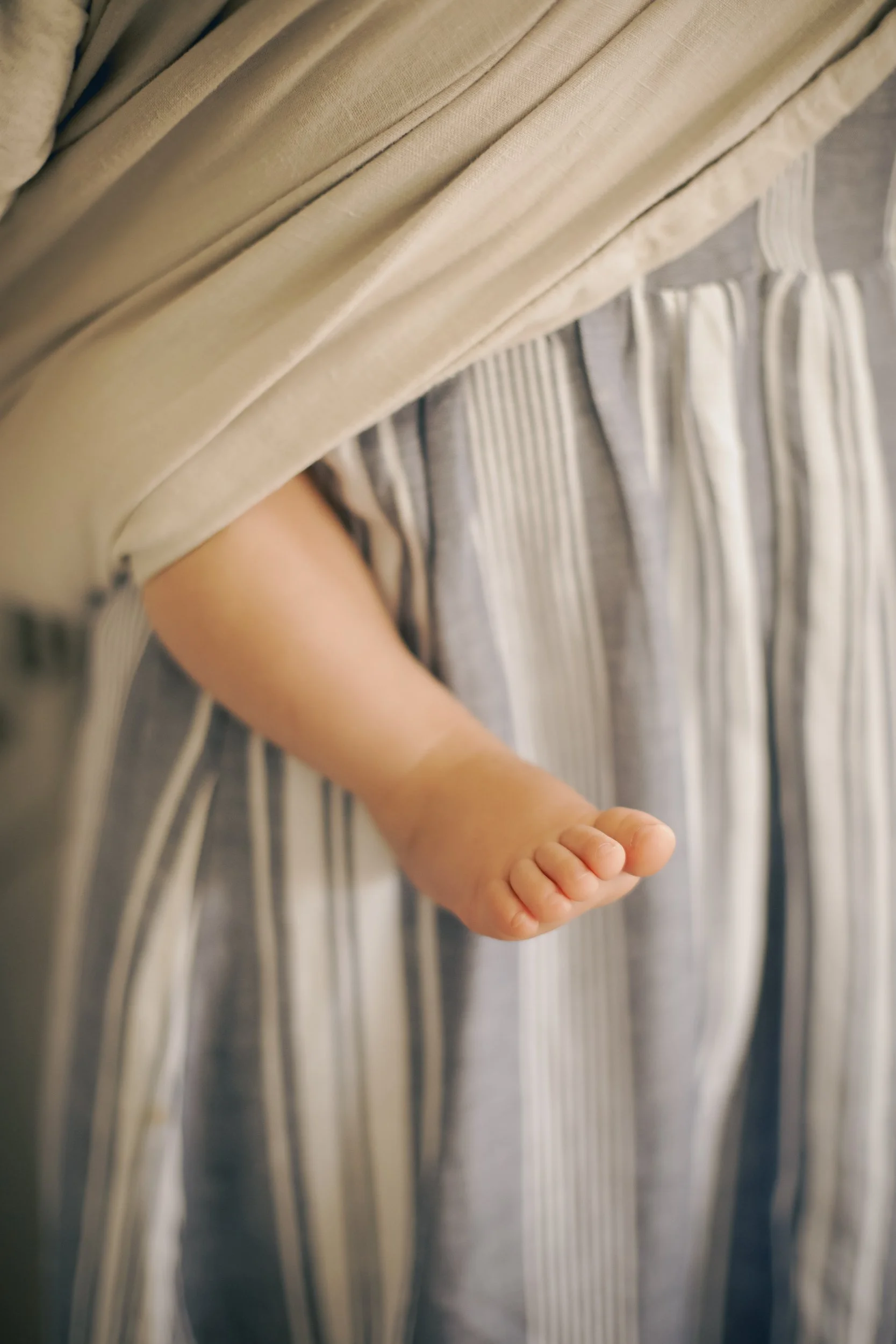 Close-up of a baby's arm and hand hanging down, draped in soft, striped fabric and cream-colored blanket.