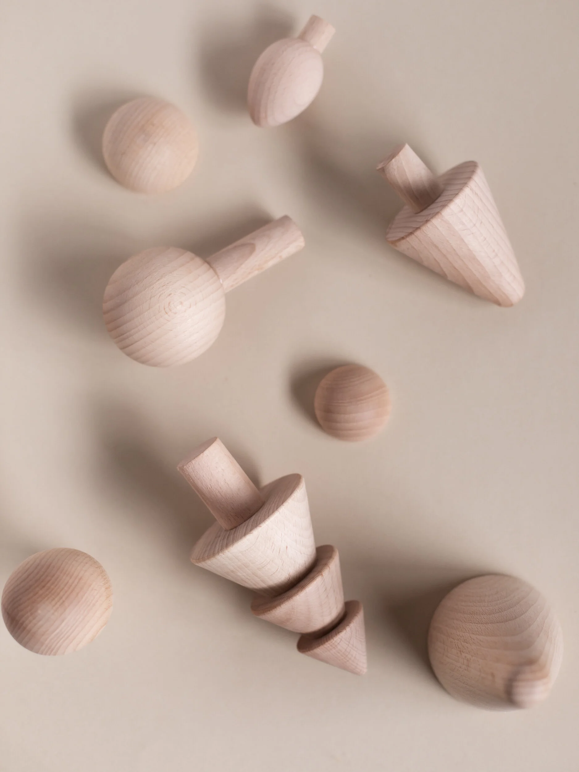 Multiple unfinished wooden geometric shapes including cones, spheres, and cylinders scattered on a plain surface.