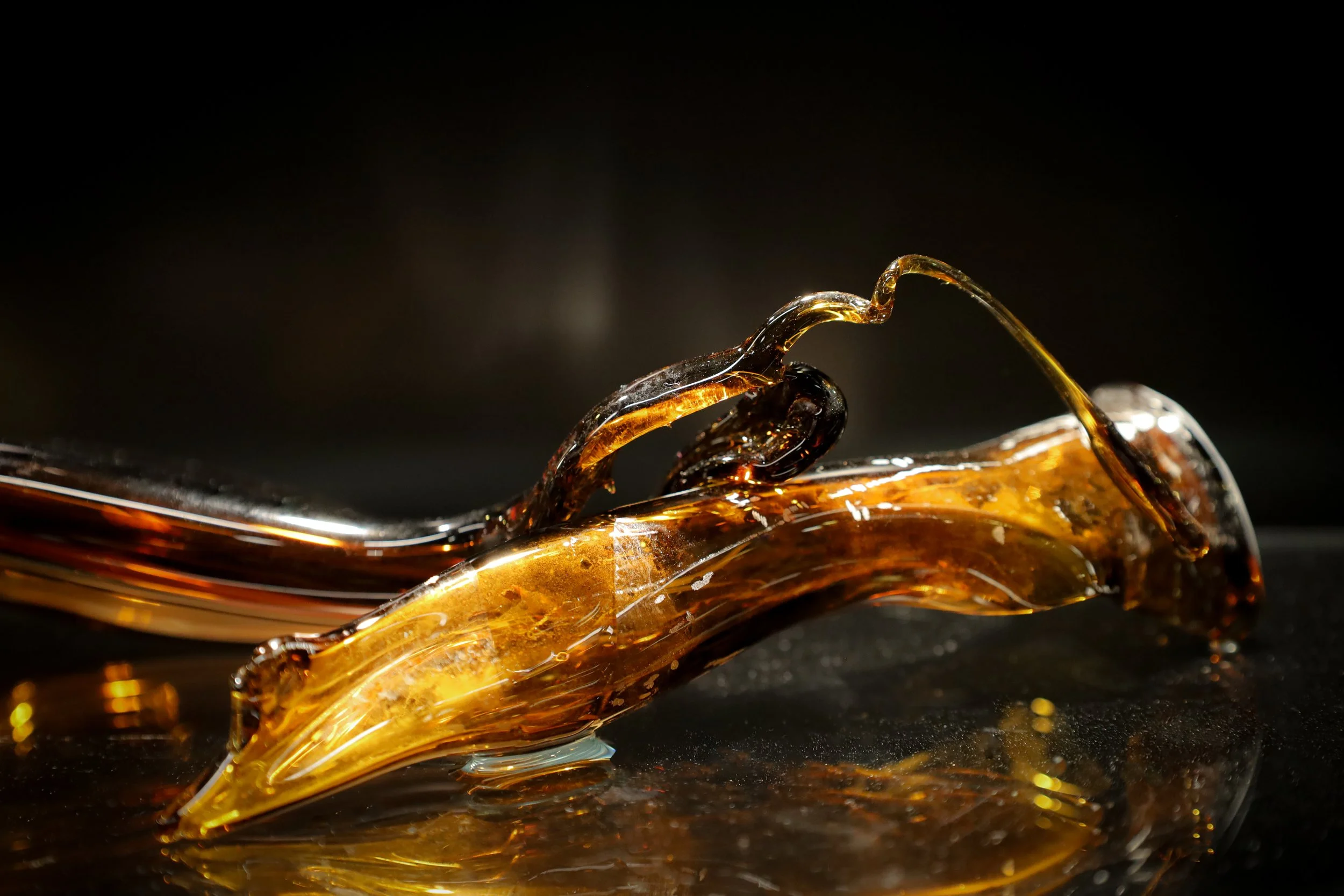 Close up of a piece of blown glass. The shape is organic and tube-like. The glass has a brown colour, with thinner areas in a light amber.