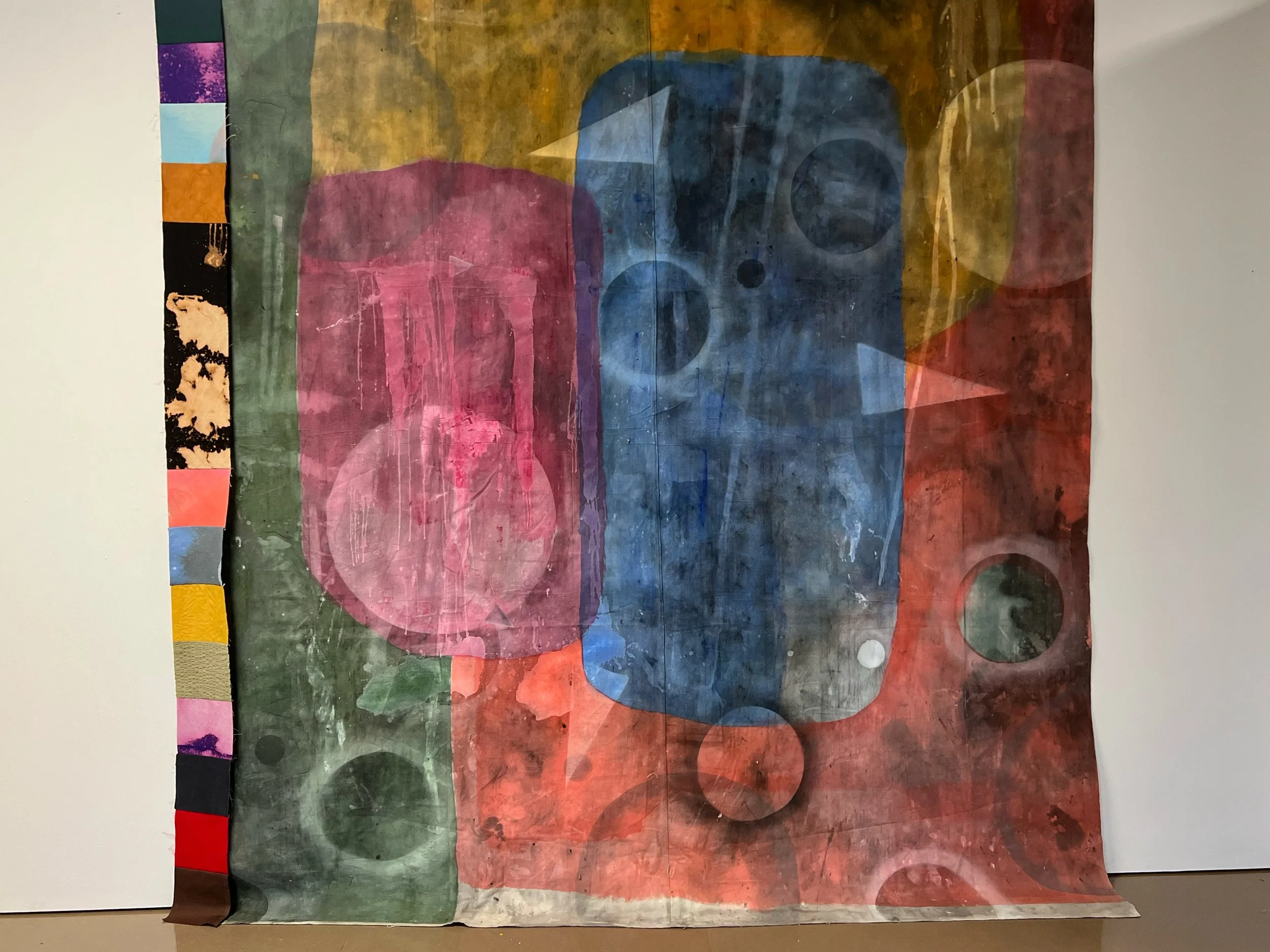 Image: Kylie Banyard, Soft wall 1, 2024. Large textile painting with patchwork fabric to the left. Several large blocks of colour, pink, red, blue, yellow and green. Circles & triangles on the painting in white and black.