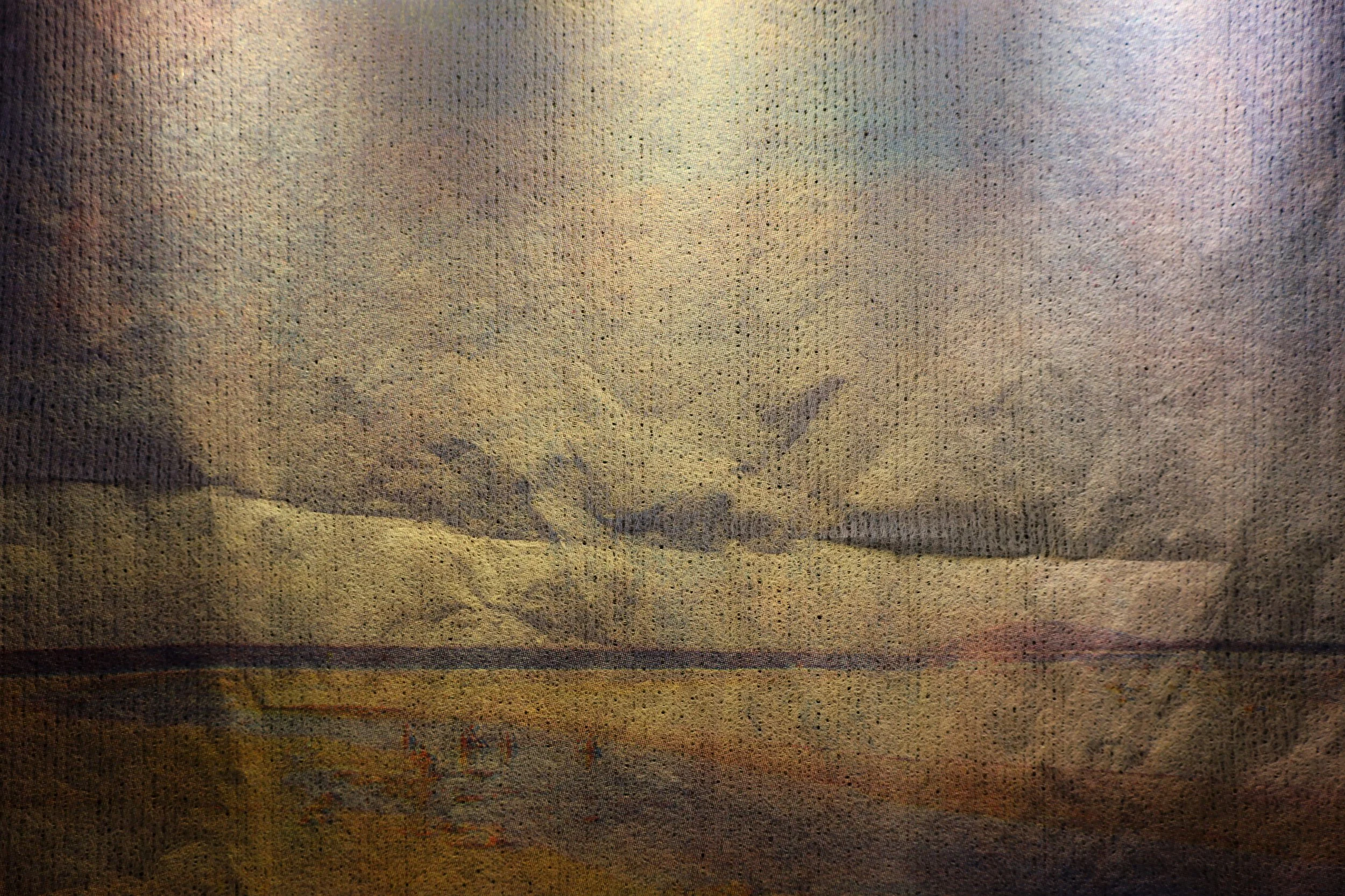 Close up view of a landscape print on textured mesh paper. The paper has folds and small holes. The image pictures clouds above a beach view, in colours of light purple, blue and yellow.