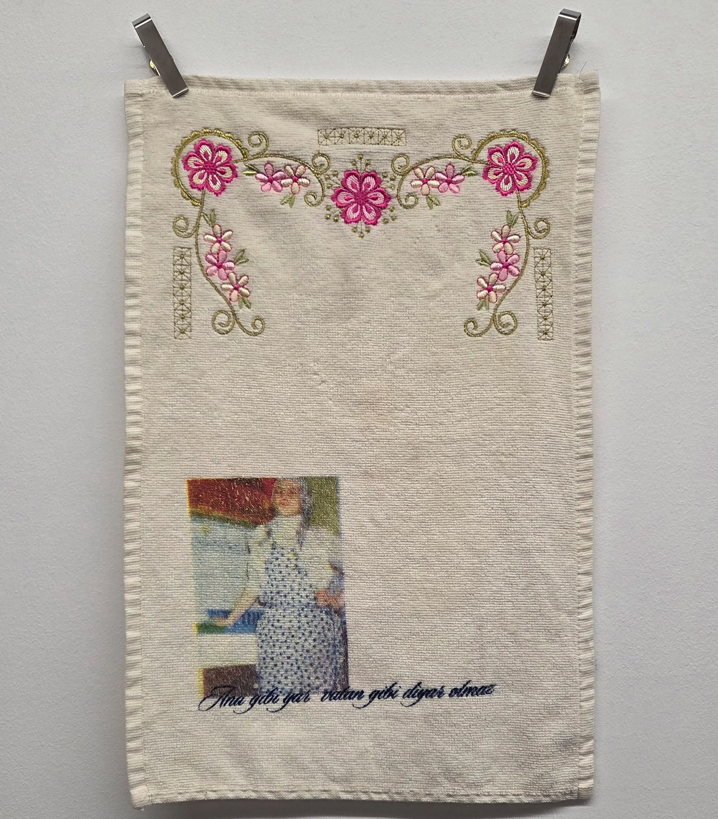 Ayesnur Kara, My mother/s tongue, 2025. Screen print on fabric with green and pink floral embroidered embellishments. The print is a small photo of a figure in an apron with black cursive script.