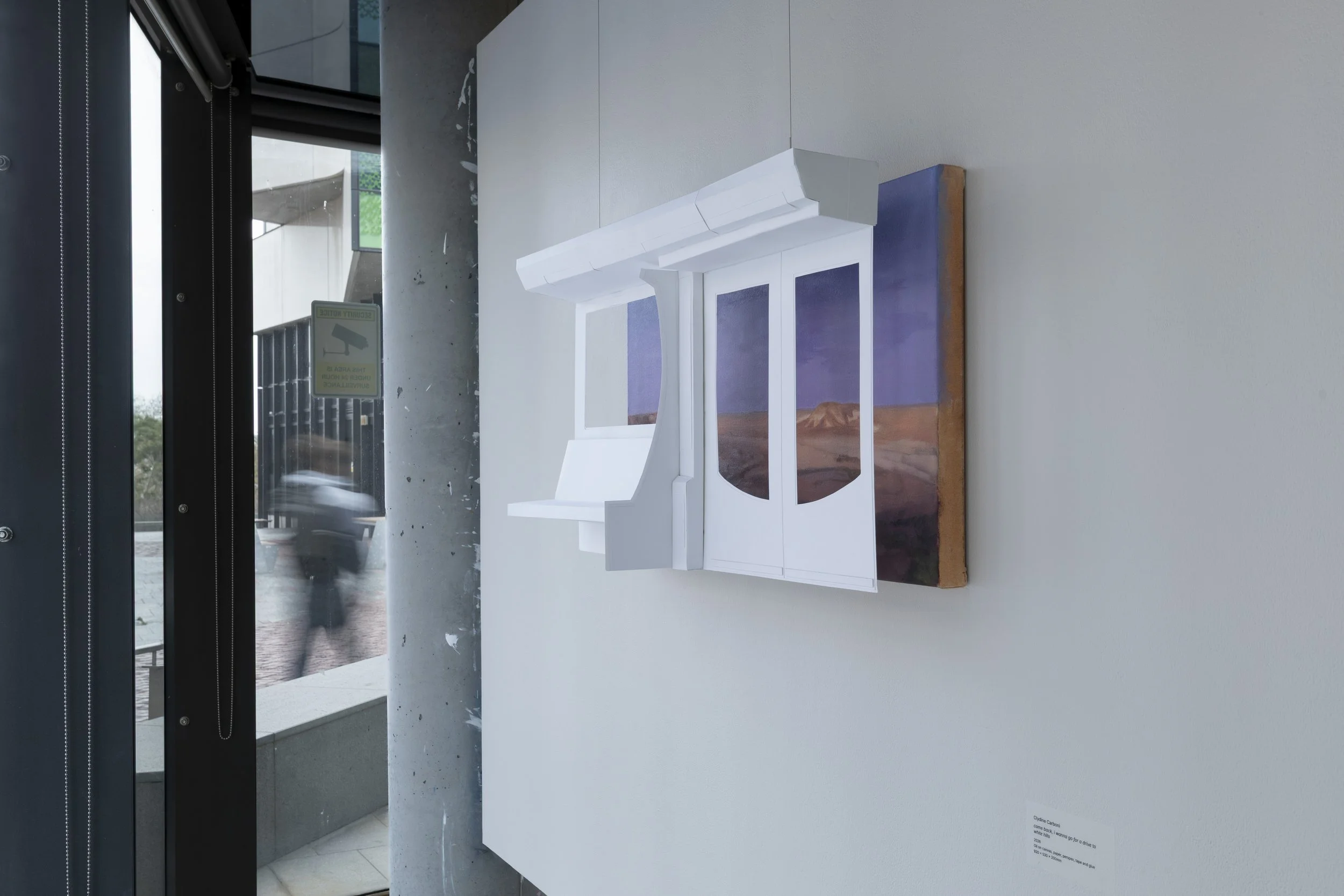 Installation view. A purple and orange landscape painting on the wall, with a white paper sculpture of a train carriage interior suspended in front, as though the painting is the view outside the train window.