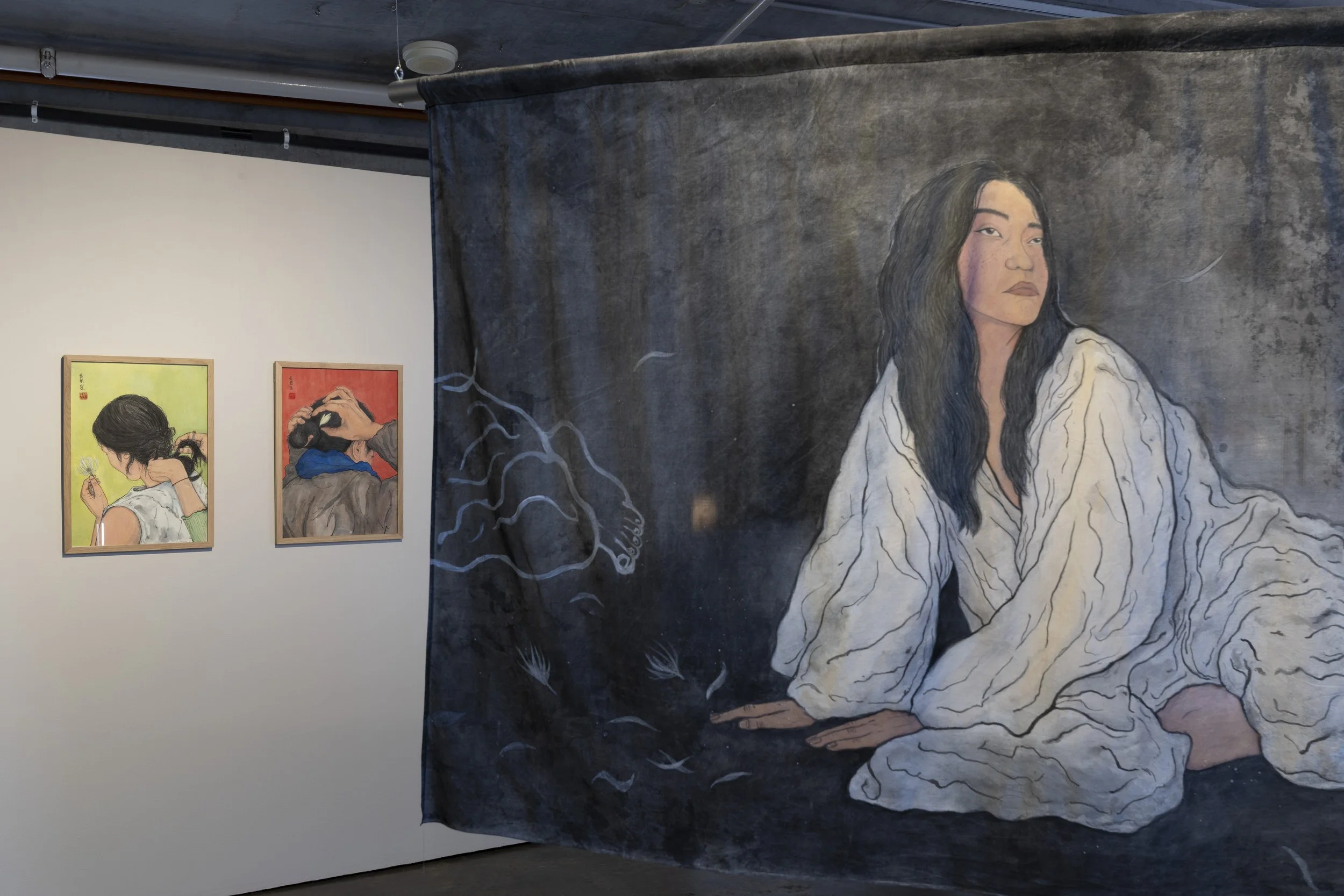 2 framed back-portraits. Left, Figure in white, holding flower, hands braiding her hair. Right, figure in black and blue tying her own hair with flower, on red. In front, hanging silk with painting of figure in white sitting.